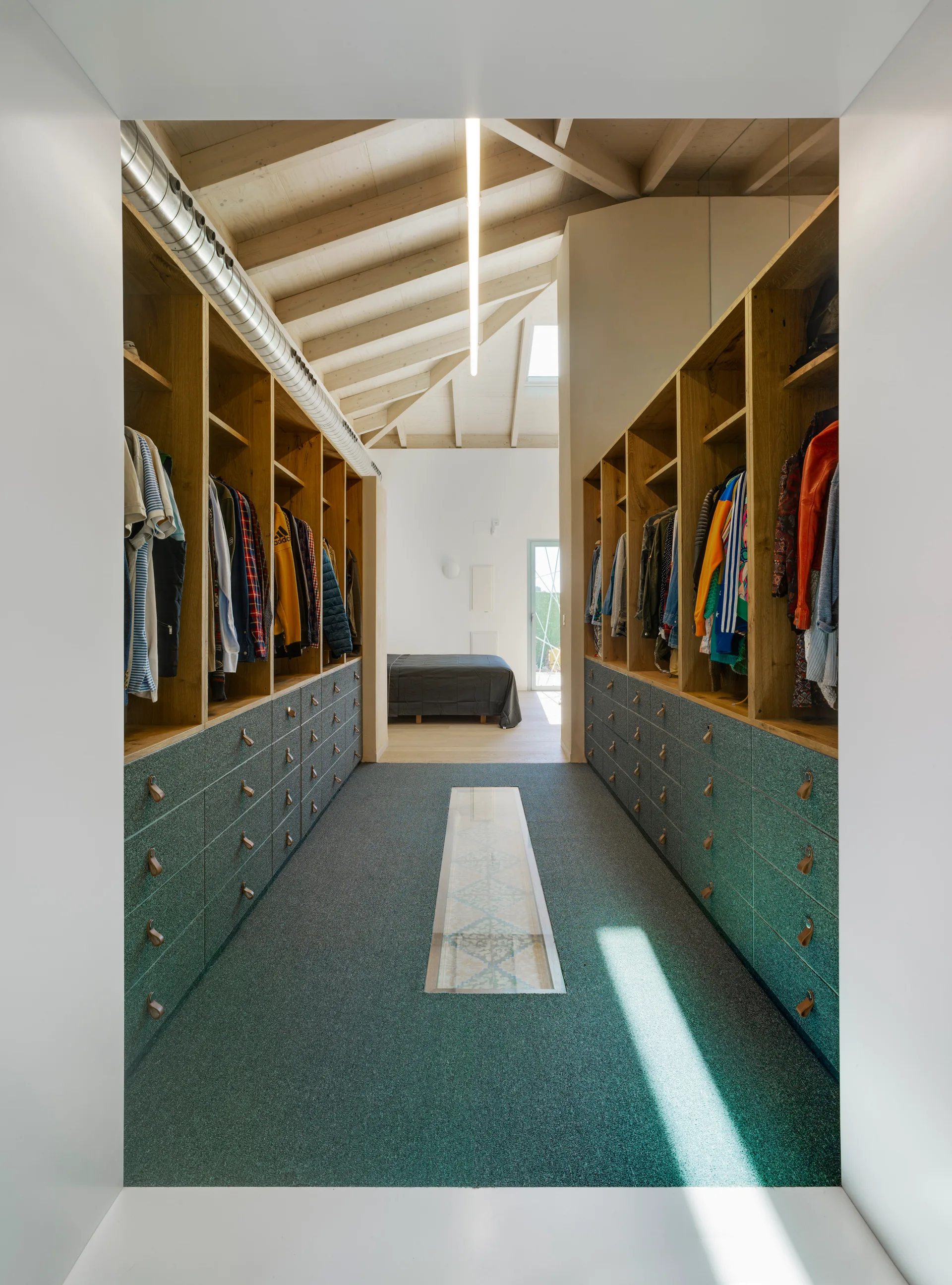A symmetrical walk-in closet featuring open wood shelving with hanging clothes above rows of green drawers under a vaulted wood ceiling.