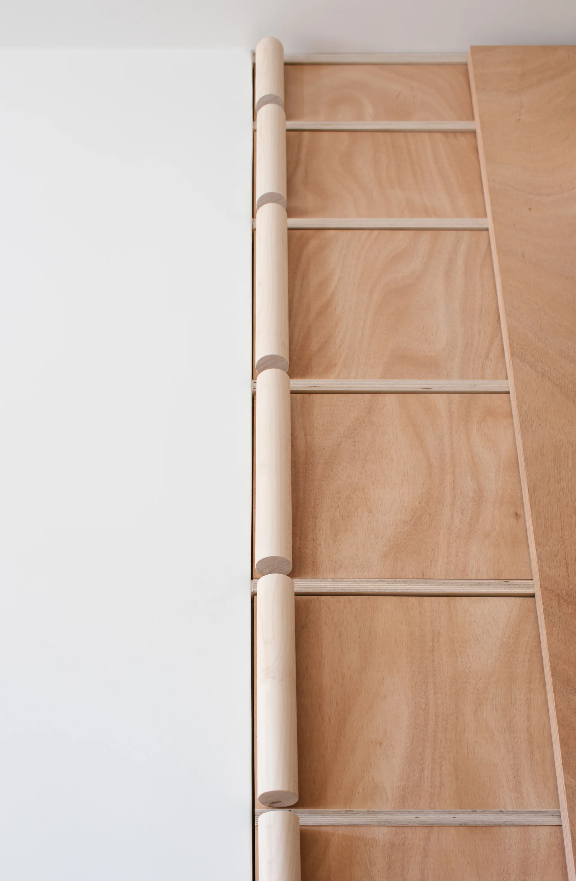 A close-up of custom light wood plywood cabinets featuring vertical wooden dowel handles next to a smooth white wall.