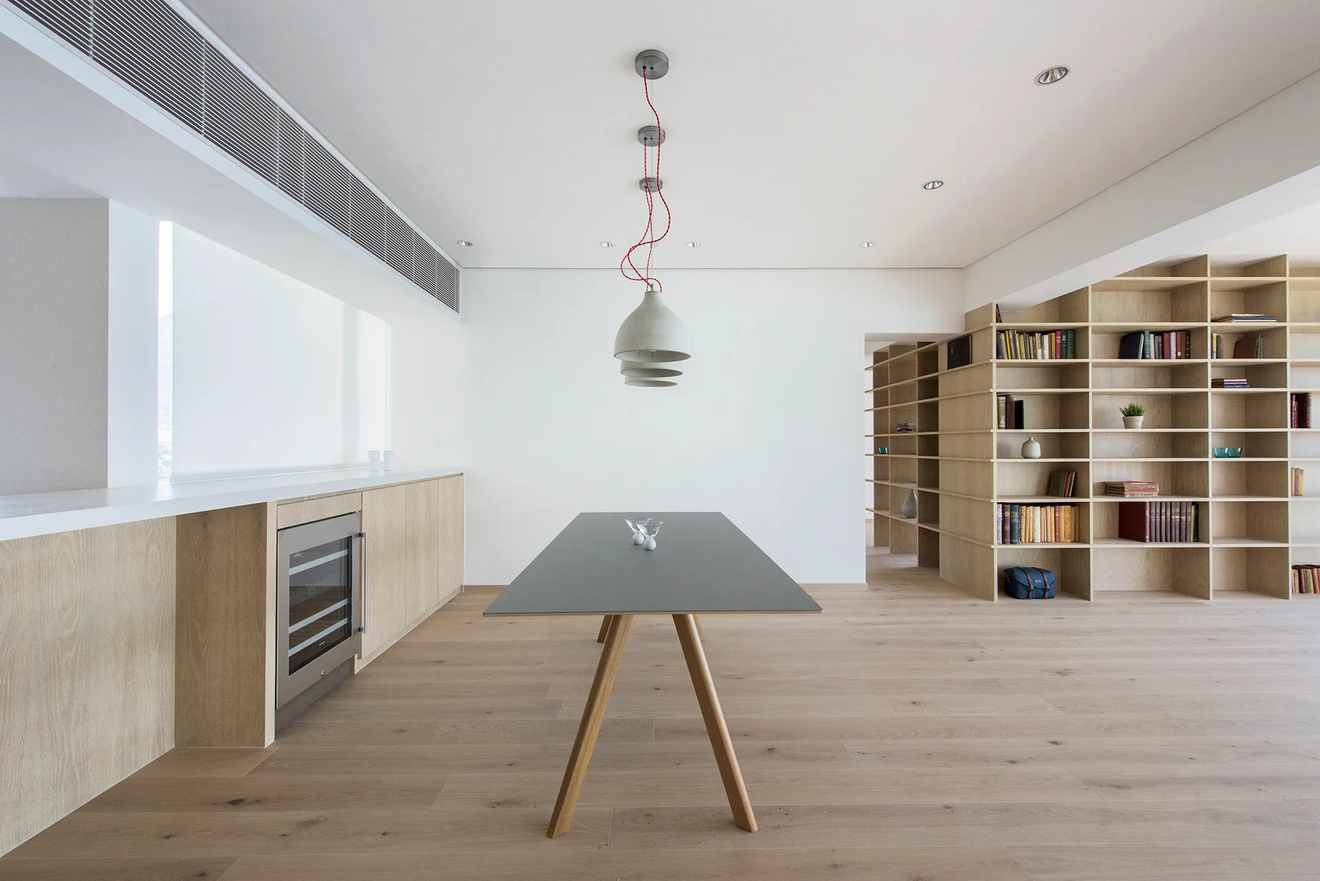 A minimalist dining area featuring a grey dining table, custom light wood grid shelving, and low cabinetry with an integrated wine cooler.