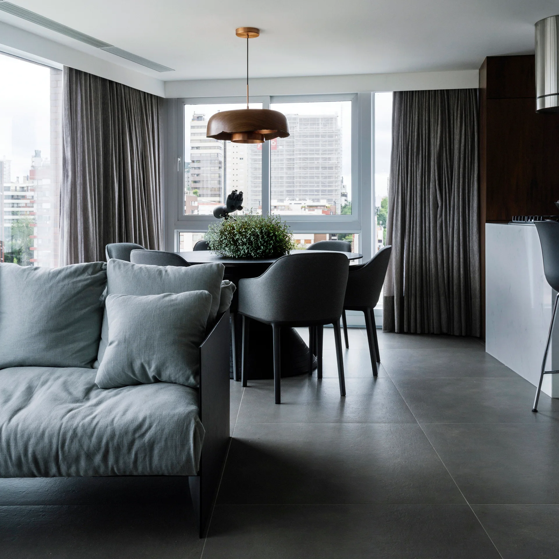 A contemporary open-plan living and dining area features a grey sofa, a round dining table with matching chairs, and a wooden dome pendant light.