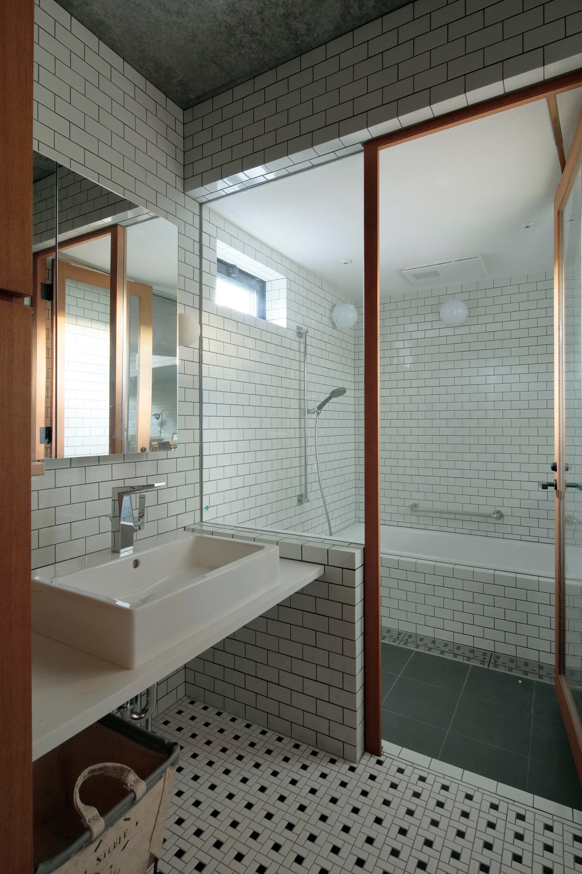 A modern bathroom features a white vessel sink on a vanity, white subway tile walls with dark grout, and a glass partition separating the shower and tub.