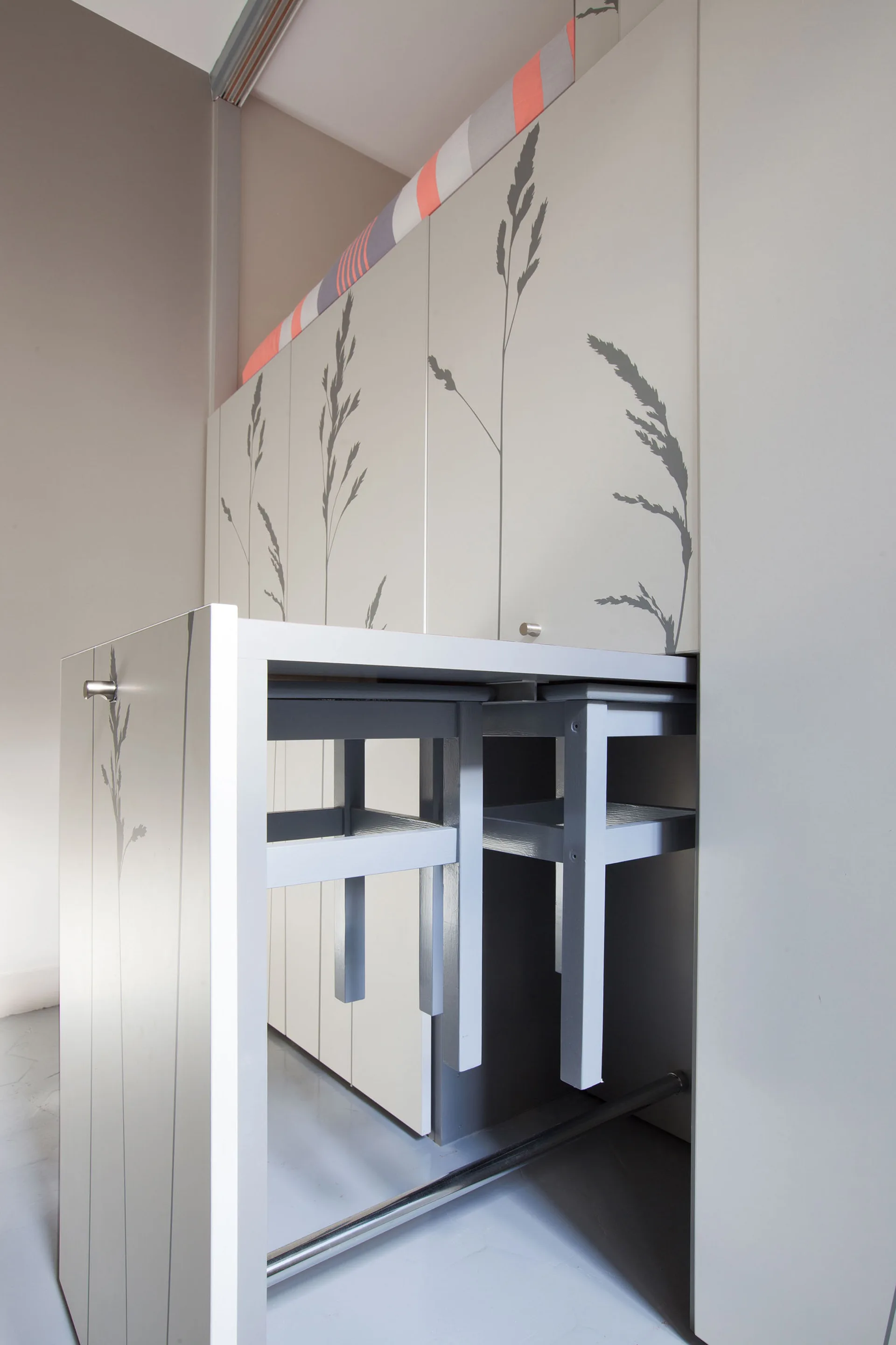 A gray pull-out dining table with two nesting stools slides out from a custom storage cabinet decorated with botanical silhouettes.