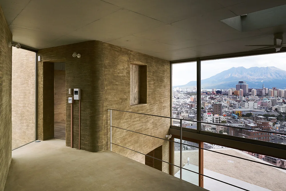A modern mezzanine corridor features rough brown textured plaster walls, smooth concrete flooring, and a large glass window showing an urban cityscape.