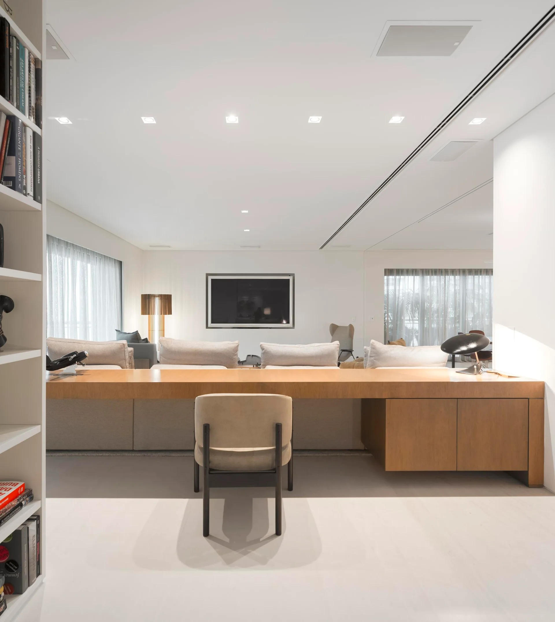 A minimalist living room features a long wood console table positioned behind a modular sofa and paired with a single upholstered armchair.