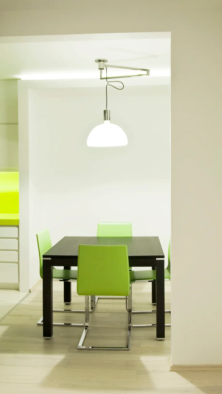 A modern dining area features a dark wood table paired with lime green cantilever chairs under a white dome pendant light.