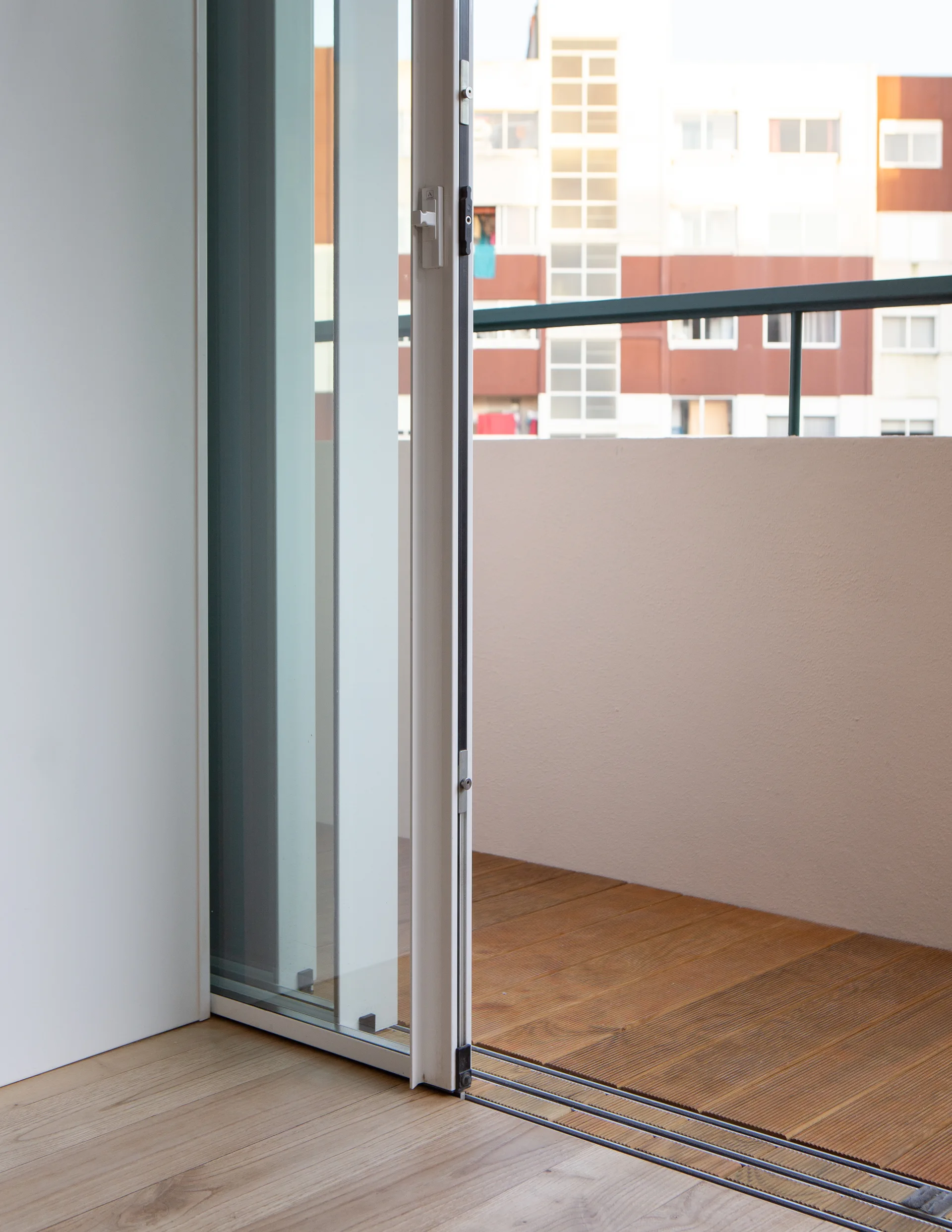 A sliding glass door with a white metal frame opens from a light wood indoor floor onto a wooden-planked balcony.