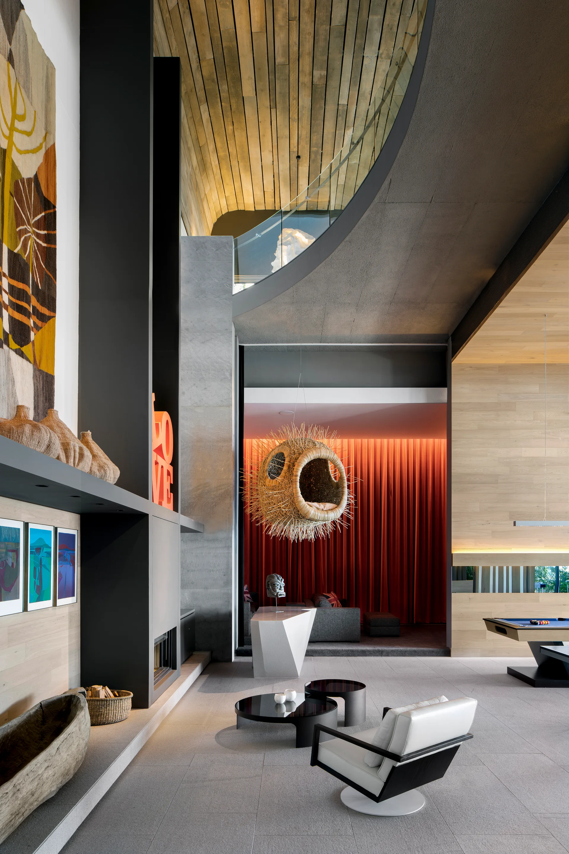 A modern living room features a curved wood plank ceiling, a tall black fireplace, grey tile floors, and a spiky woven hanging chair in the background.