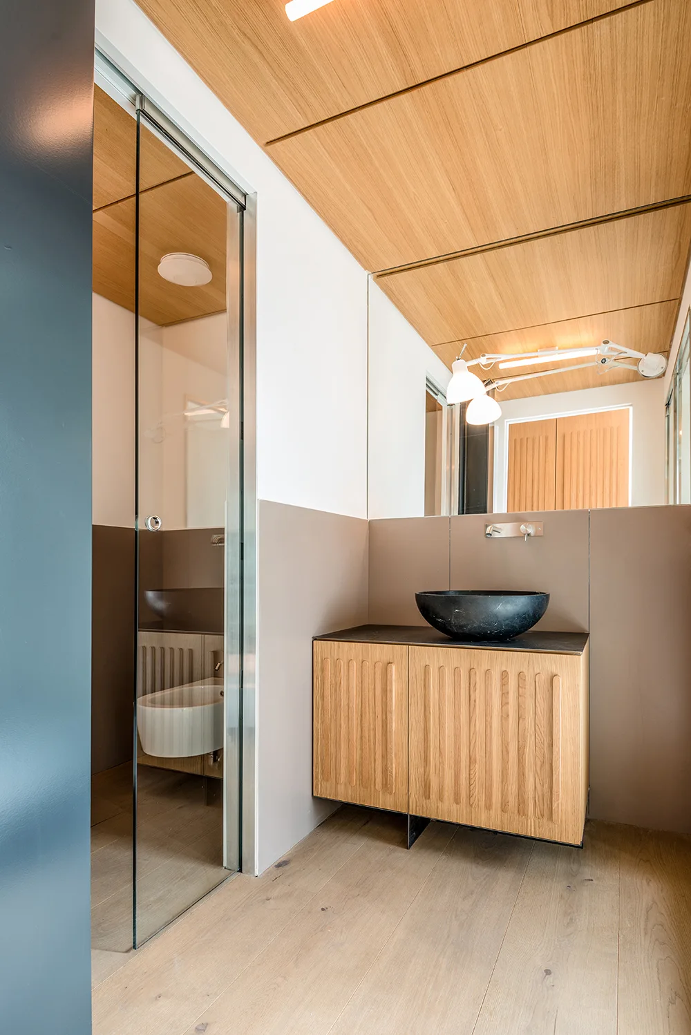 A modern bathroom featuring a fluted wood vanity with a black vessel sink, a large mirror, and a matching wood paneled ceiling.