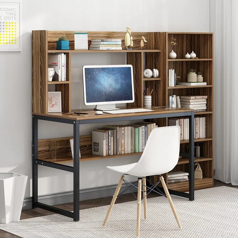 A wood-toned desk with a black metal frame and built-in shelving hutch is paired with a white molded plastic chair in a bright room.