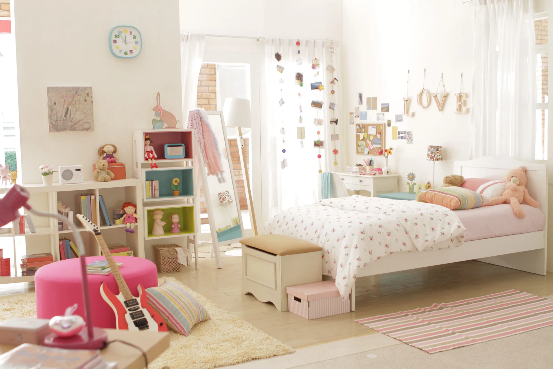 A bright children's bedroom with a white wooden bed, pastel storage cubbies, and a pink ottoman on a shag rug.