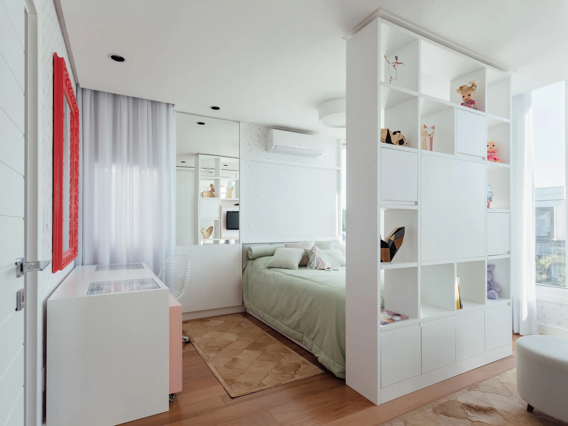 A modern bedroom features a white floor-to-ceiling shelving unit acting as a room divider next to a bed with light green bedding.
