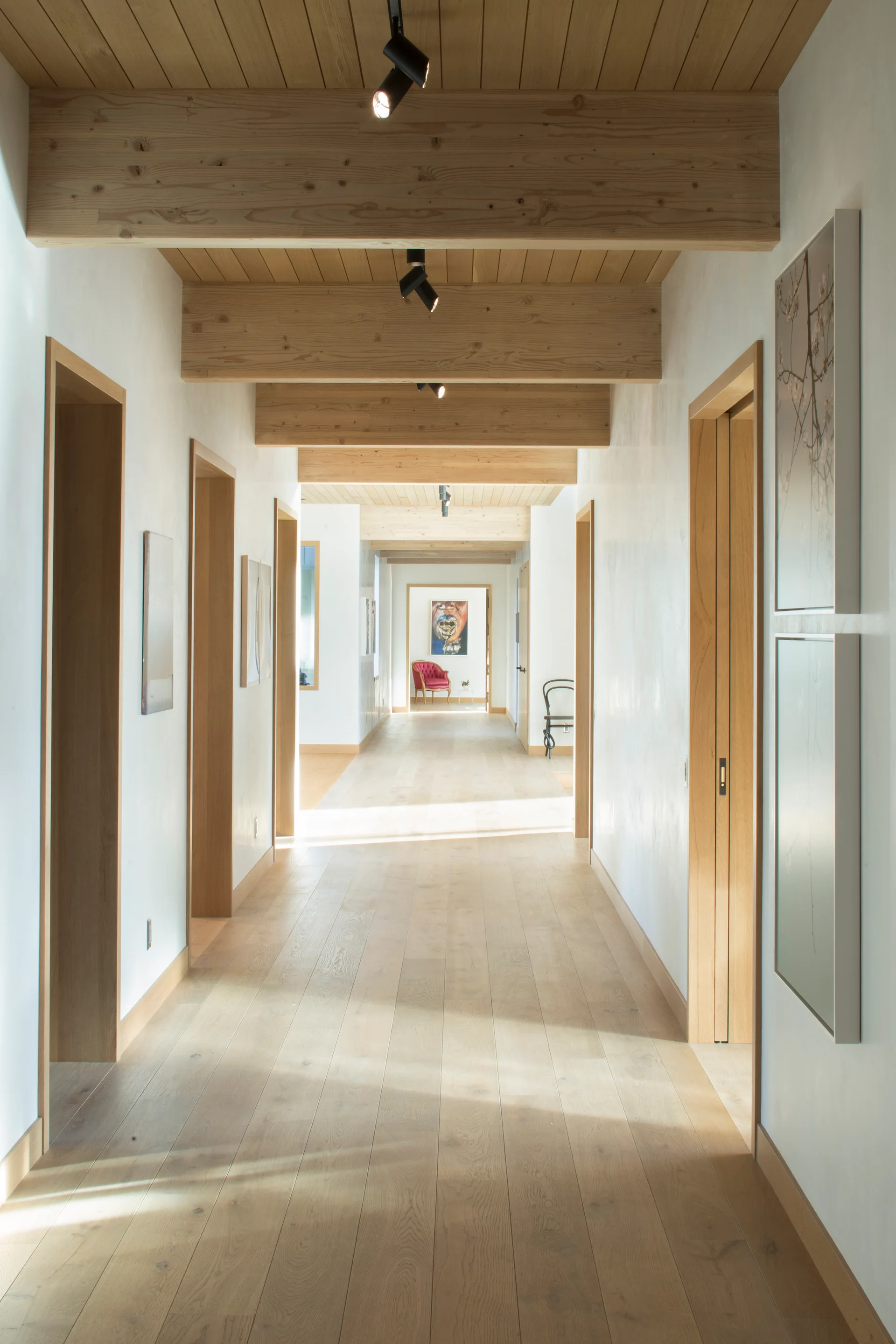 A long residential hallway features light wood plank flooring, a matching wood ceiling with exposed beams, and multiple doorways.