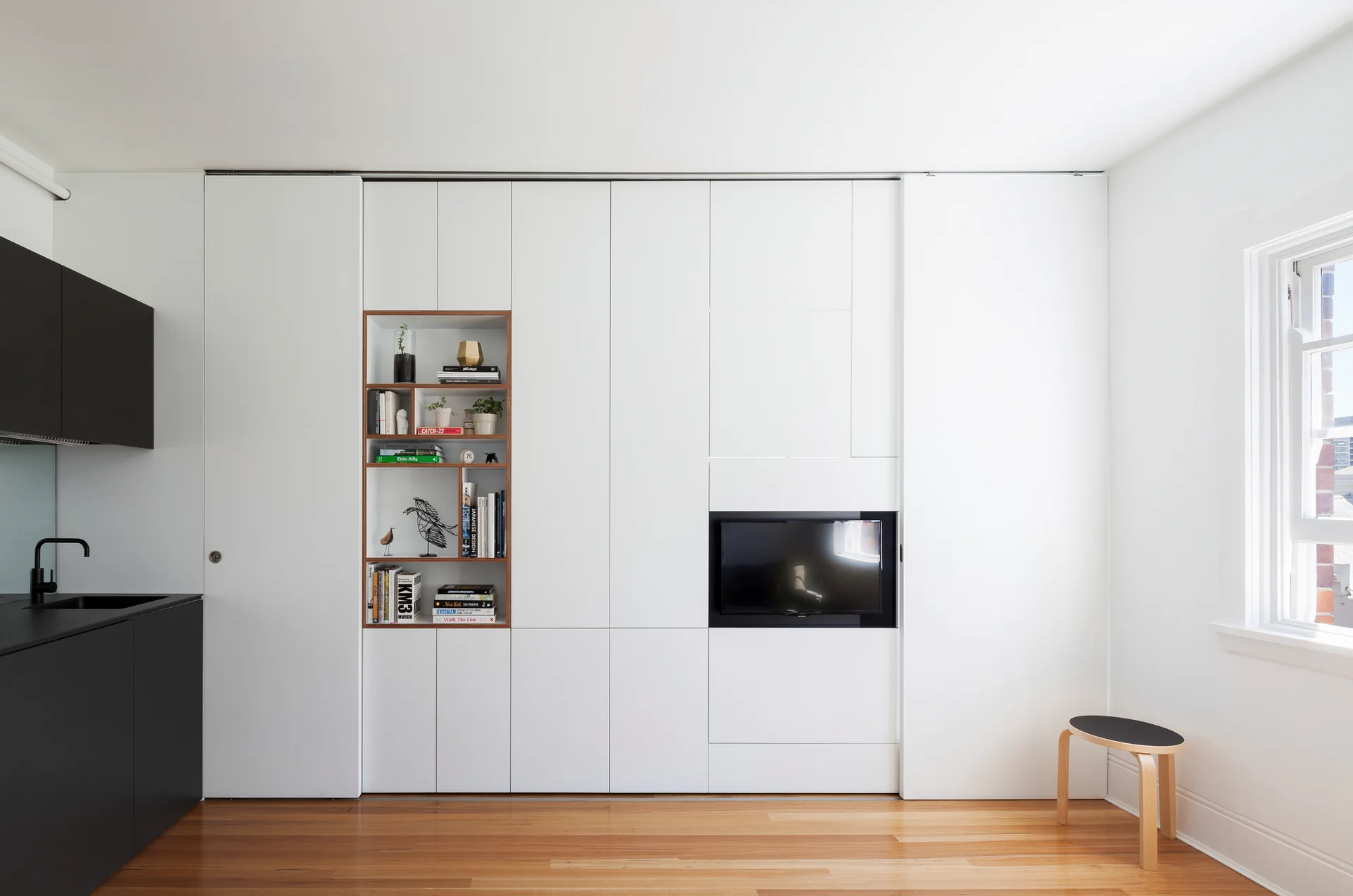 A seamless white storage wall features an integrated wood-framed shelf unit and a built-in television above wood flooring.