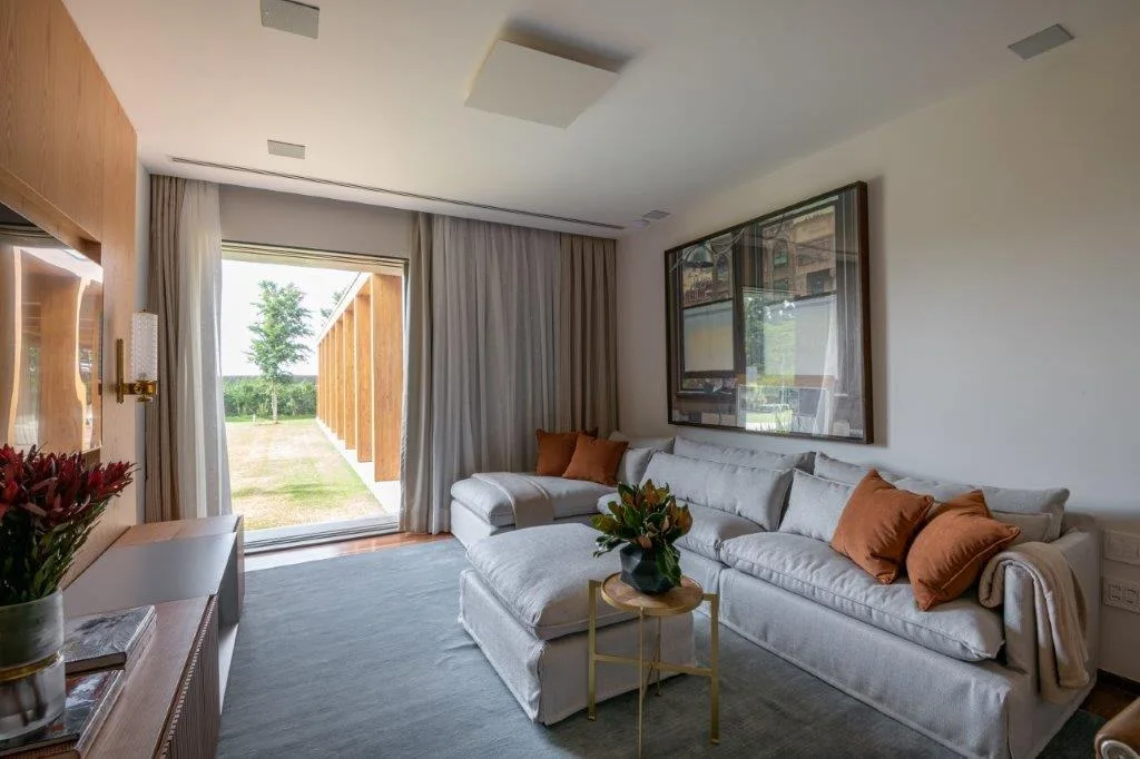 A modern living room features a grey sectional sofa with rust-colored pillows, a large area rug, and wood wall paneling next to glass doors.