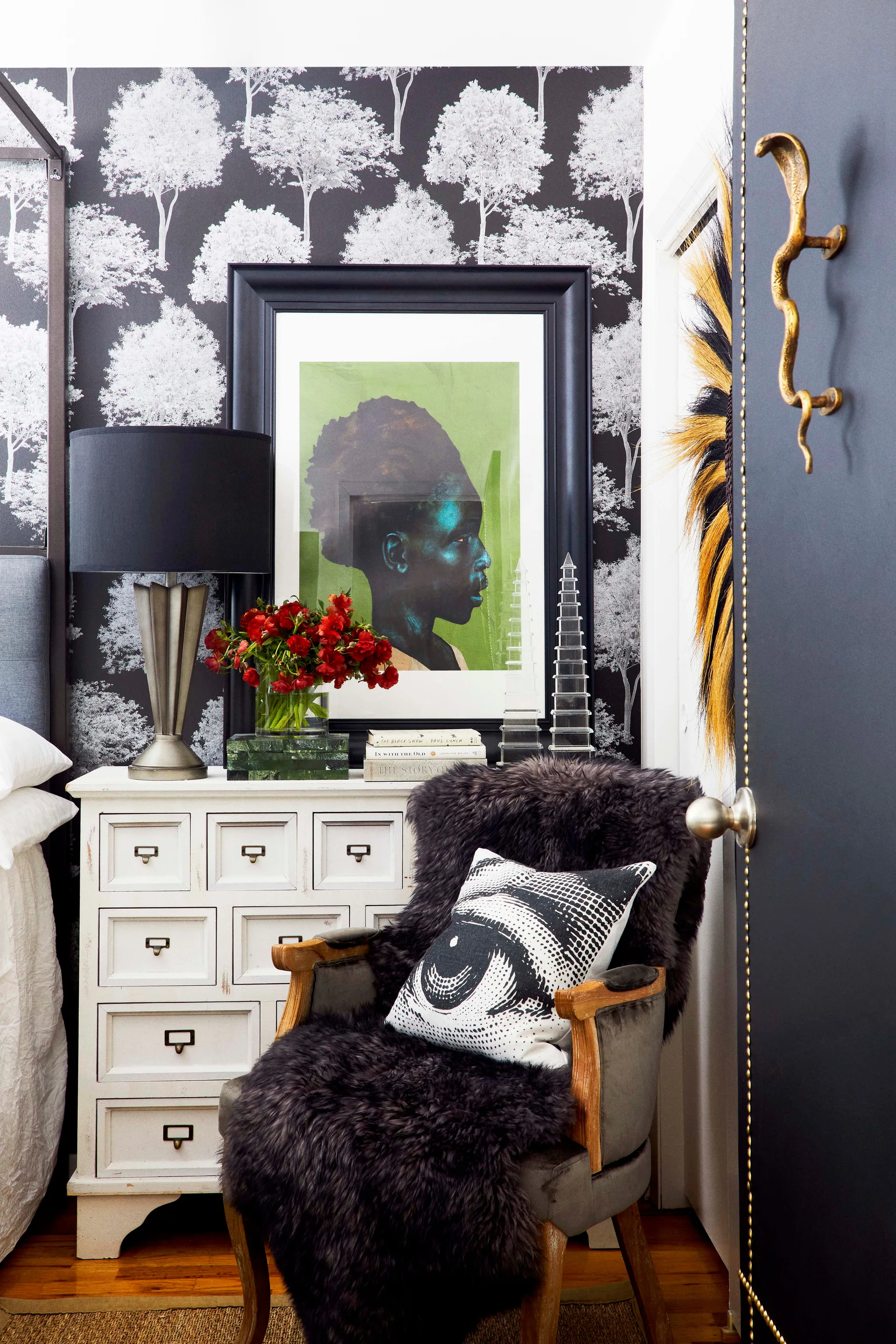 A bedroom corner features black and white tree wallpaper, a white multi-drawer dresser with framed artwork, and an armchair draped in a dark fur throw.