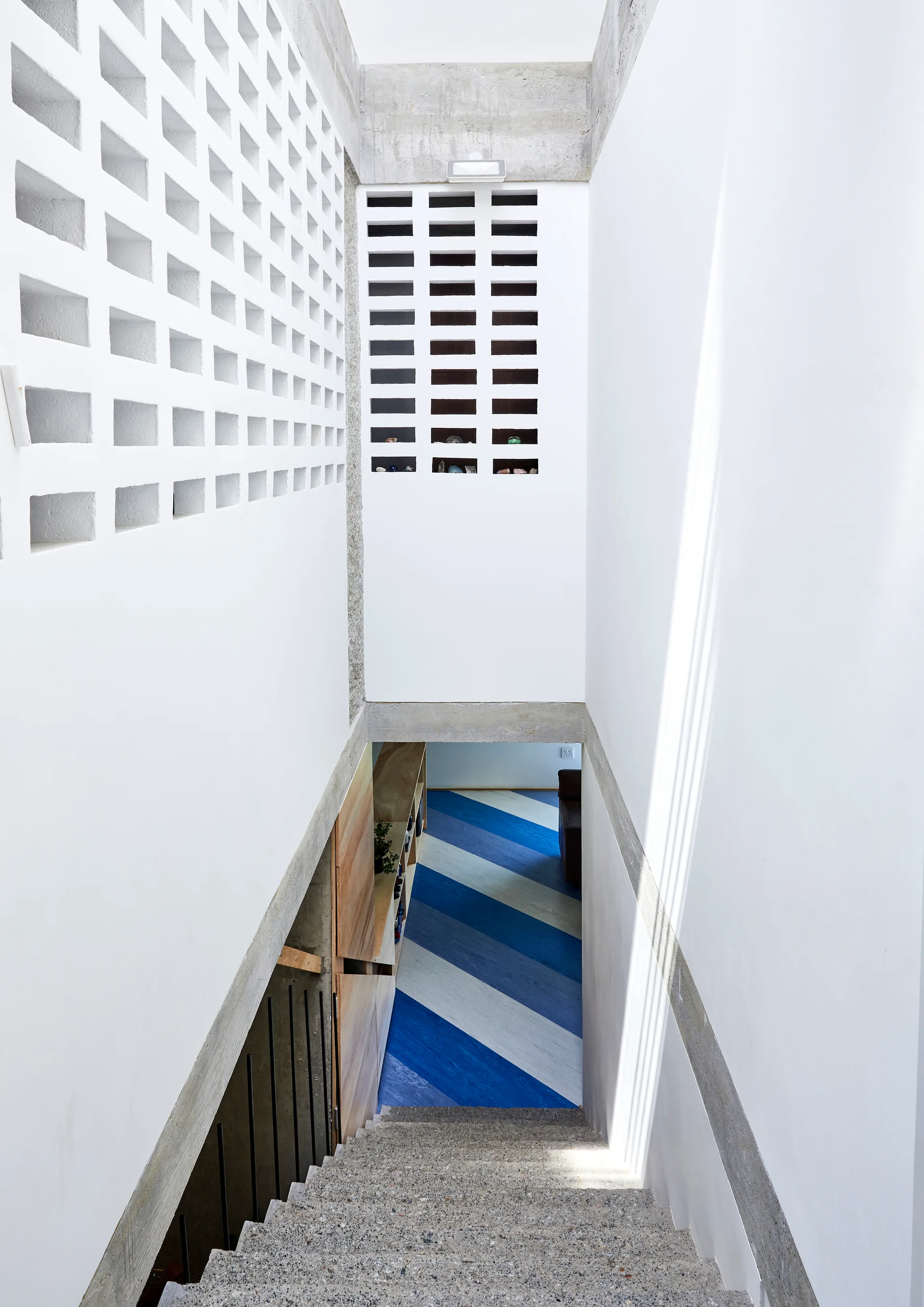 A concrete staircase descends past white breezeblock screen walls toward a landing with a blue and white striped diagonal pattern.