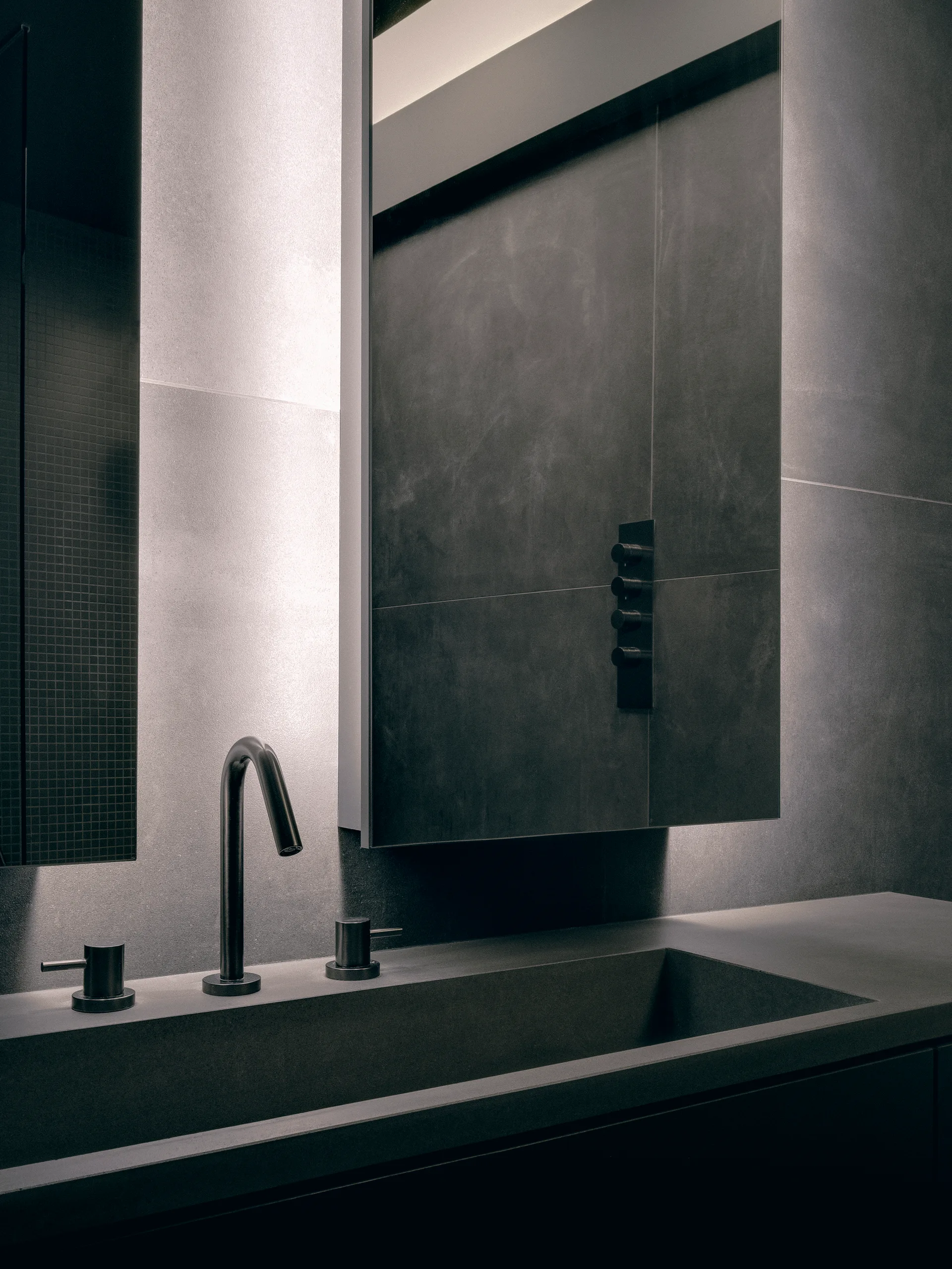 A modern dark grey bathroom vanity featuring a matte charcoal integrated basin, black faucet, and a large backlit recessed mirror.