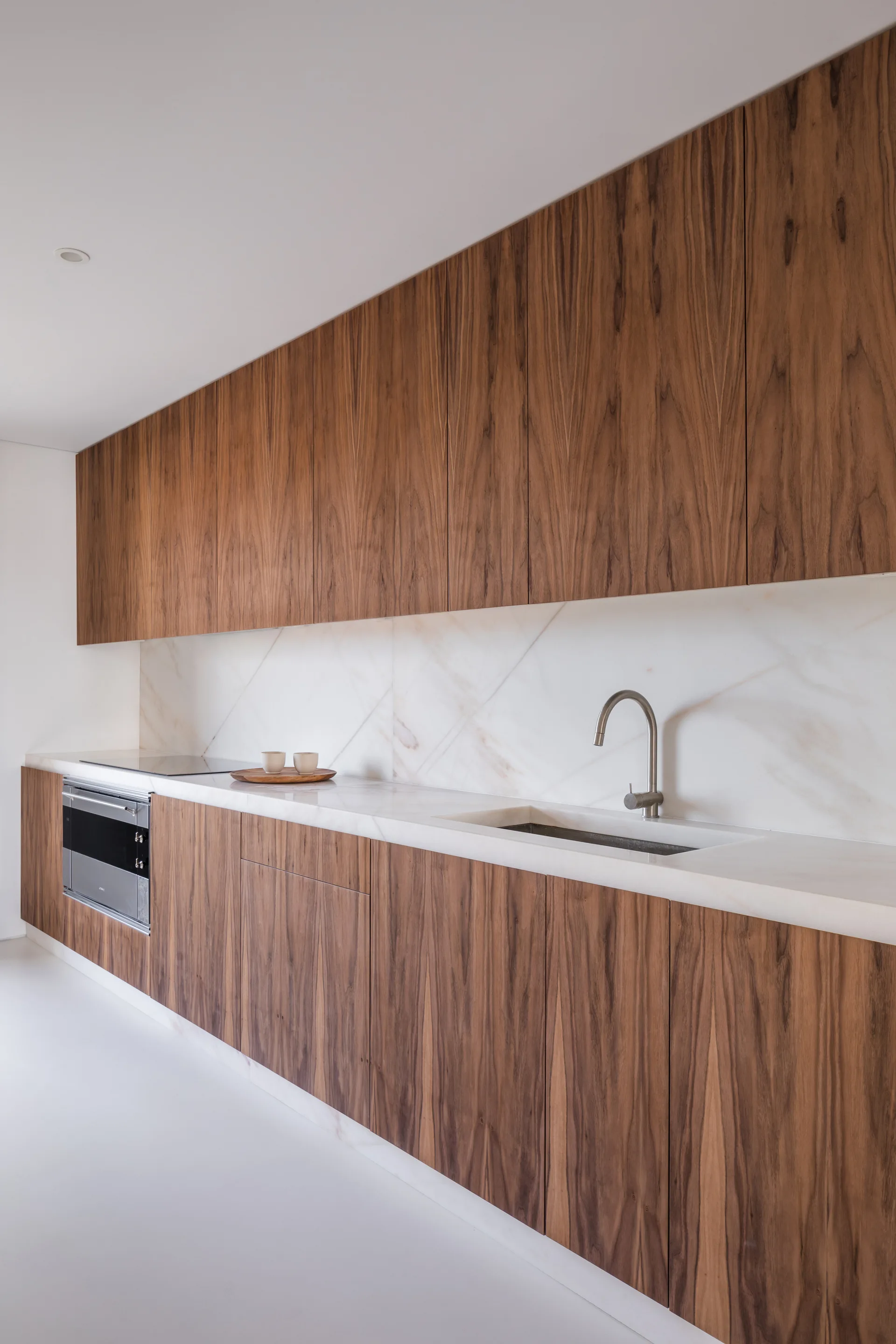 Minimalist kitchen featuring flat-panel wood cabinetry, a white marble countertop and backsplash, an integrated sink, and a built-in oven.