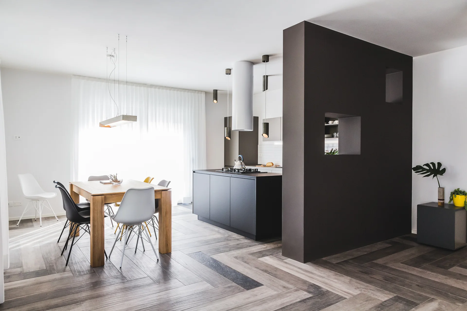 An open-concept kitchen and dining area features a dark partition wall, a wood dining table with modern chairs, and herringbone-patterned flooring.