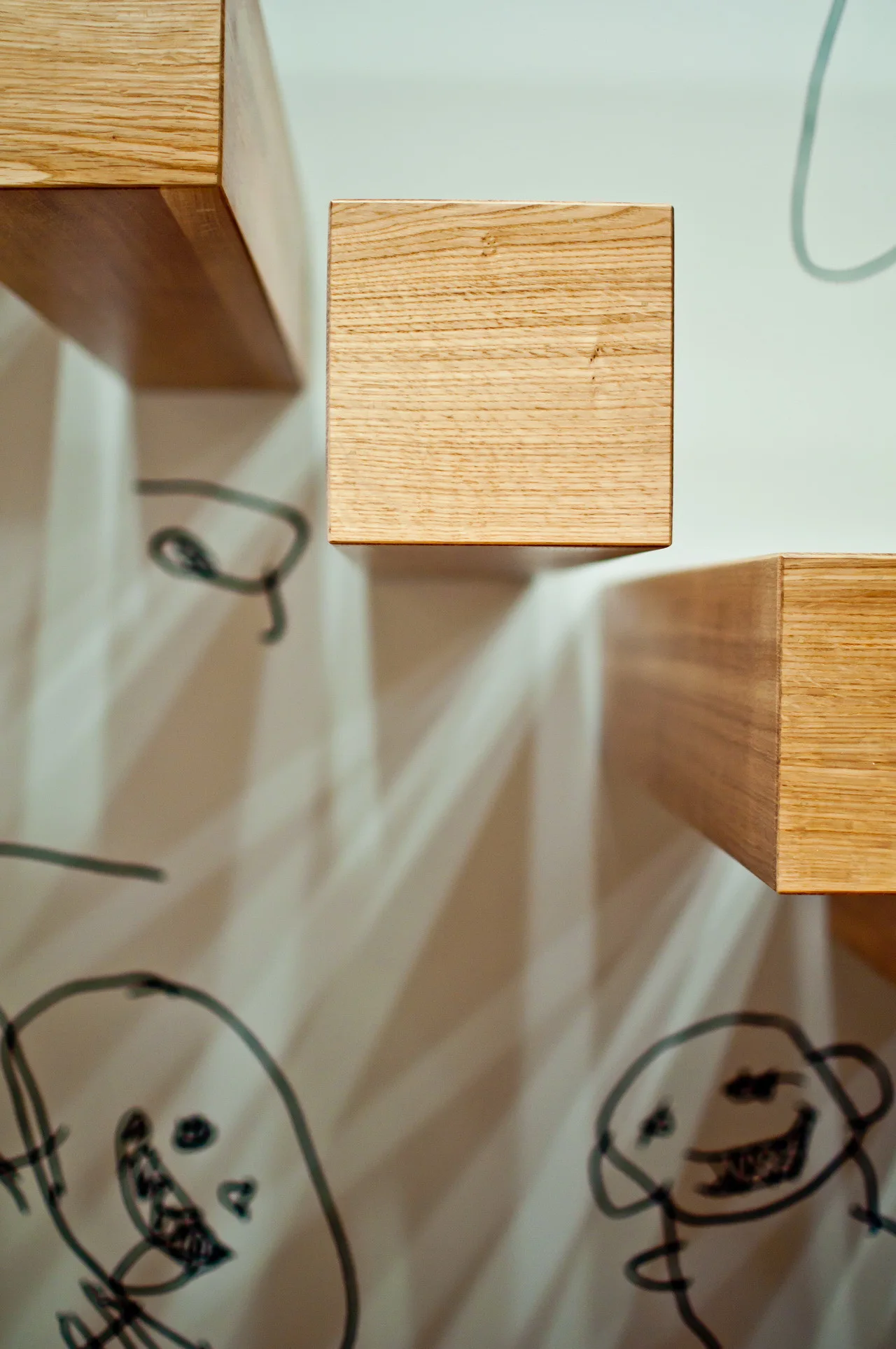 Close-up of minimalist floating wooden box stair treads mounted on a white wall featuring hand-drawn black line art doodles.