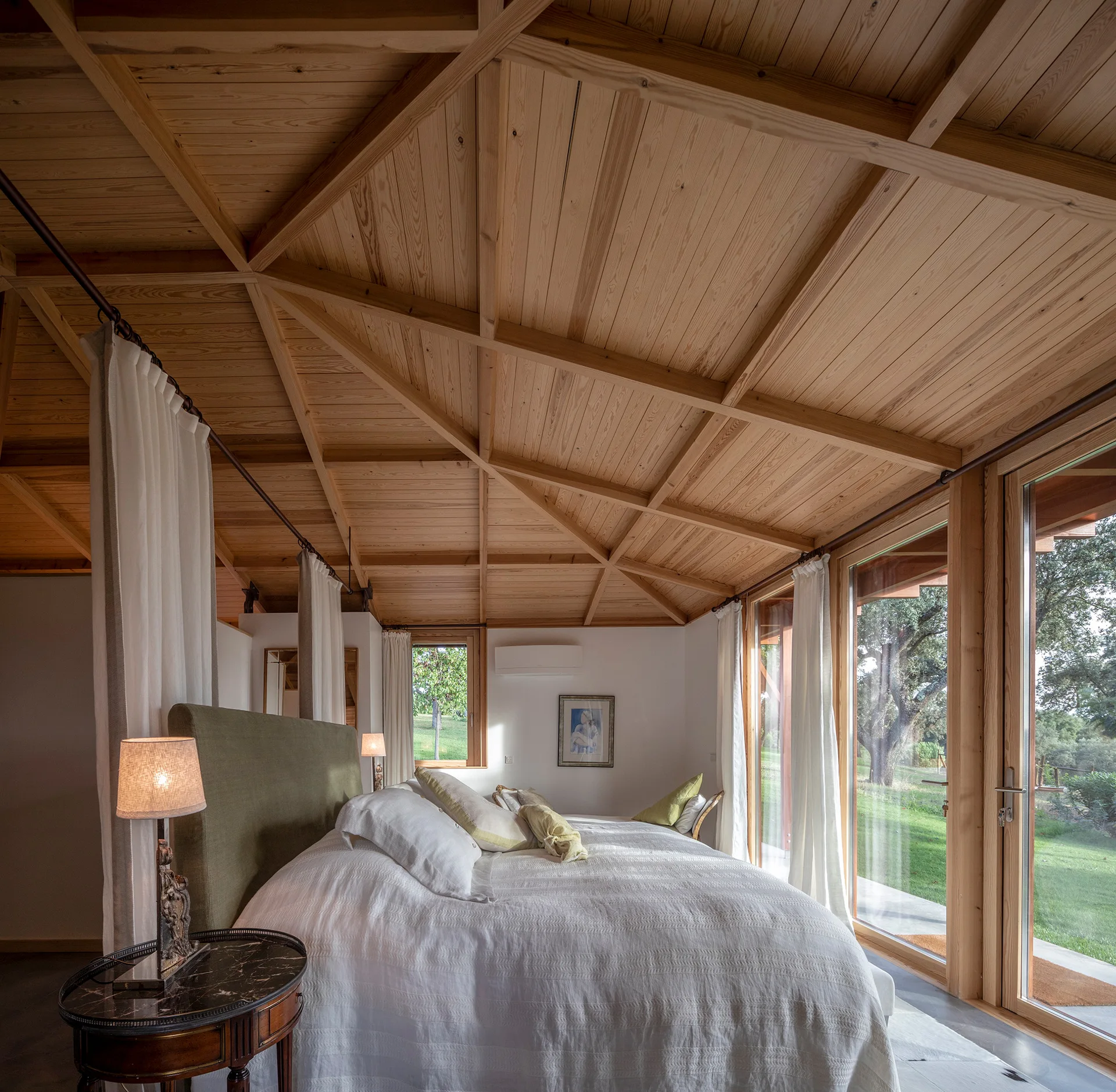 A bedroom featuring an intricate geometric wood ceiling, a bed with a green headboard, and large glass sliding doors opening to a grassy yard.