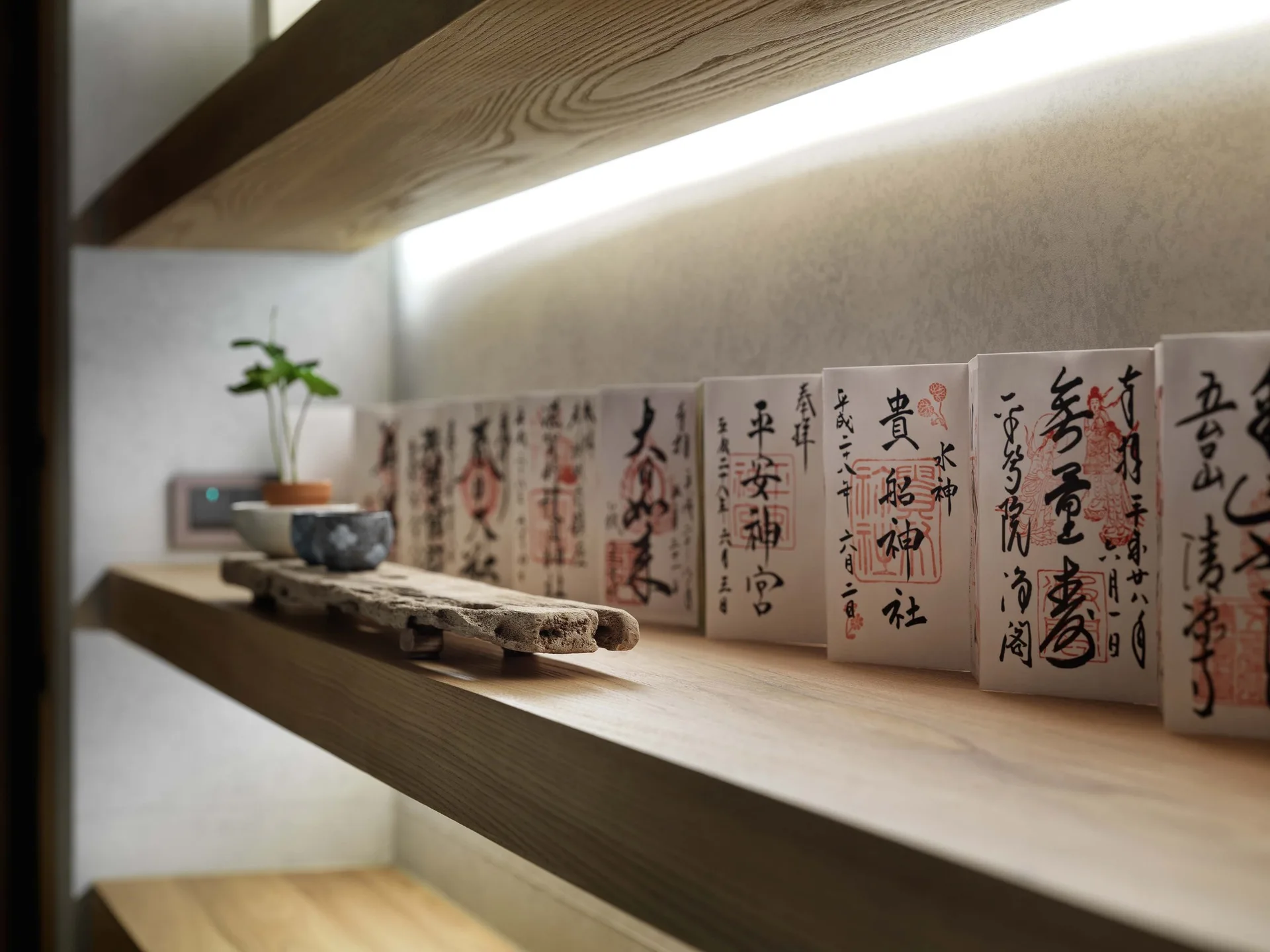 A close-up view of a light wood floating shelf illuminated by a warm LED light strip and displaying decorative calligraphy cards.