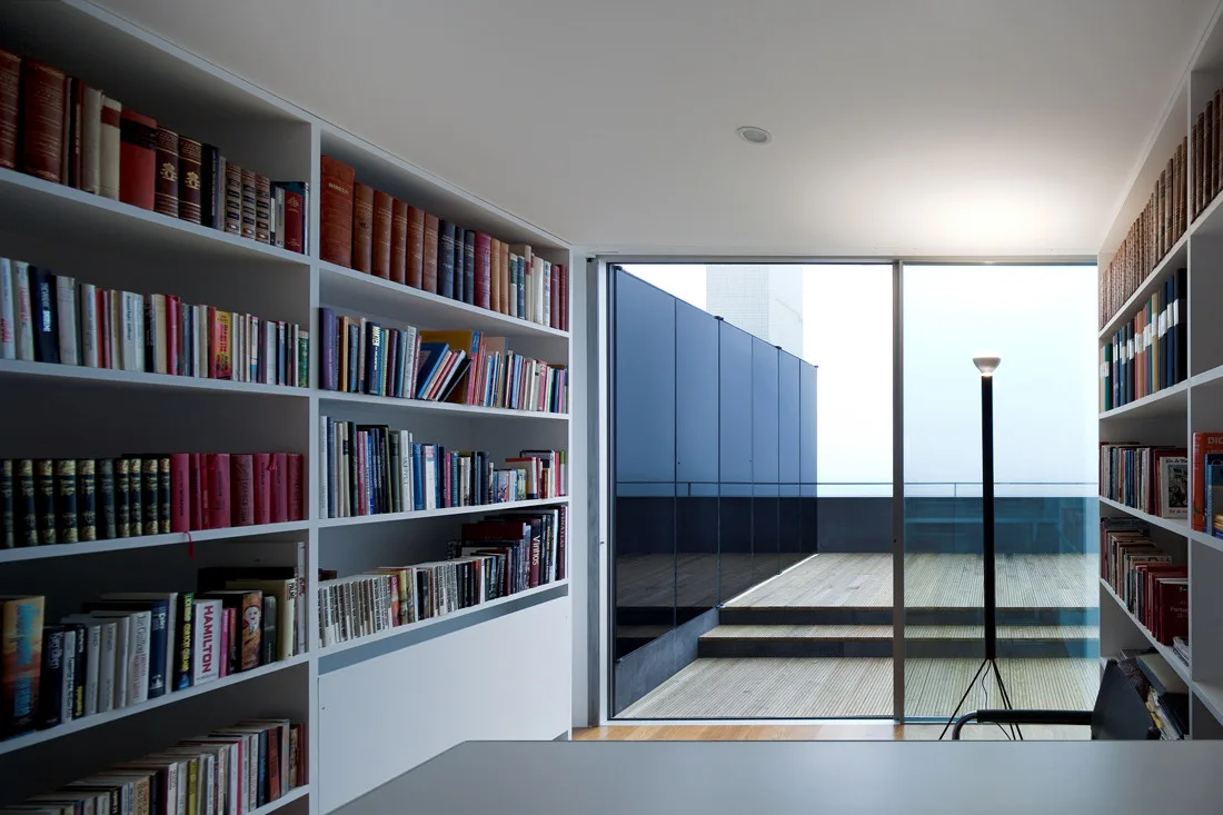 A home library featuring white floor-to-ceiling bookshelves and a large glass sliding door leading to an outdoor wooden terrace.