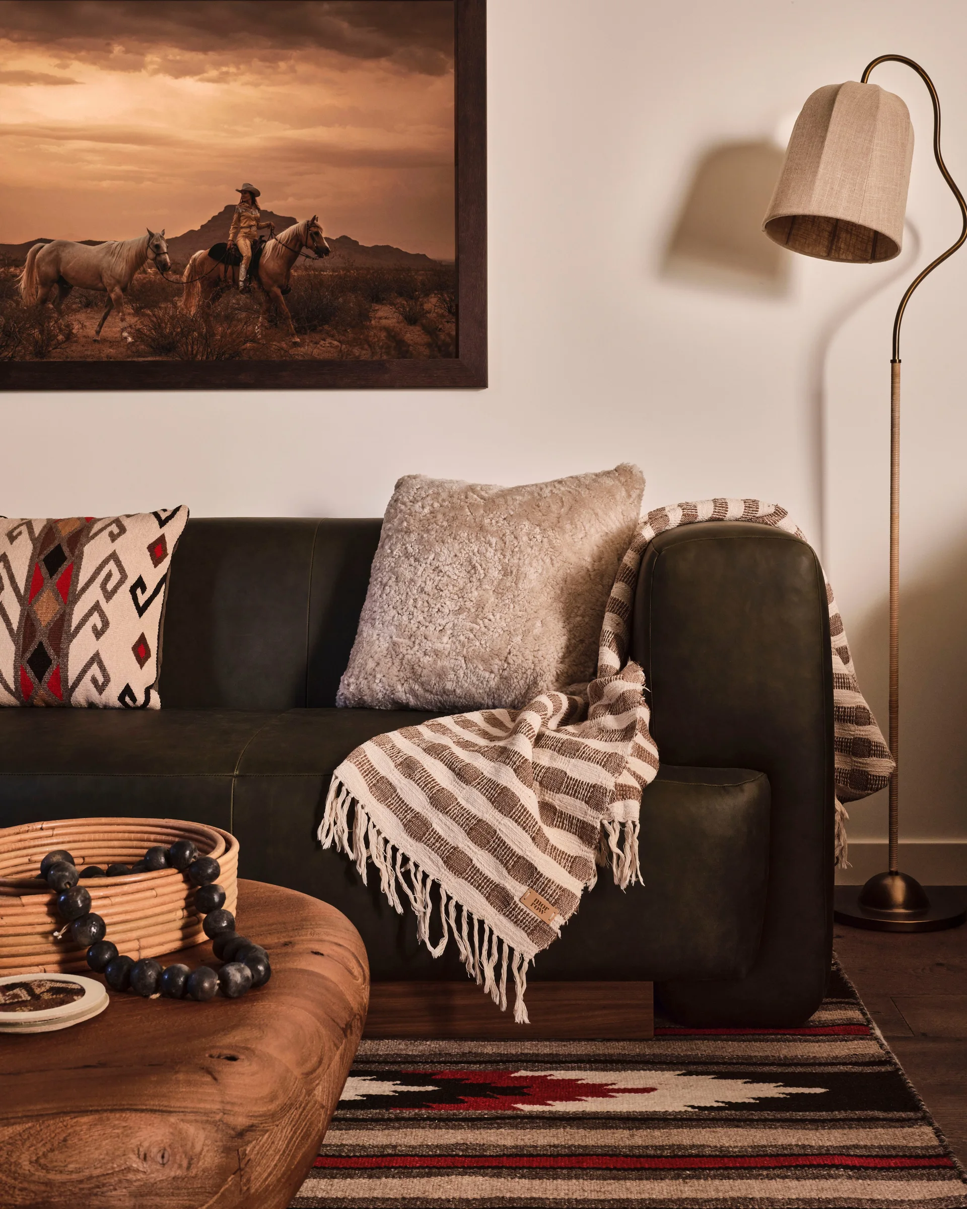 A dark green leather sofa features a Southwestern patterned pillow and striped throw blanket next to a round wooden coffee table and warm floor lamp.