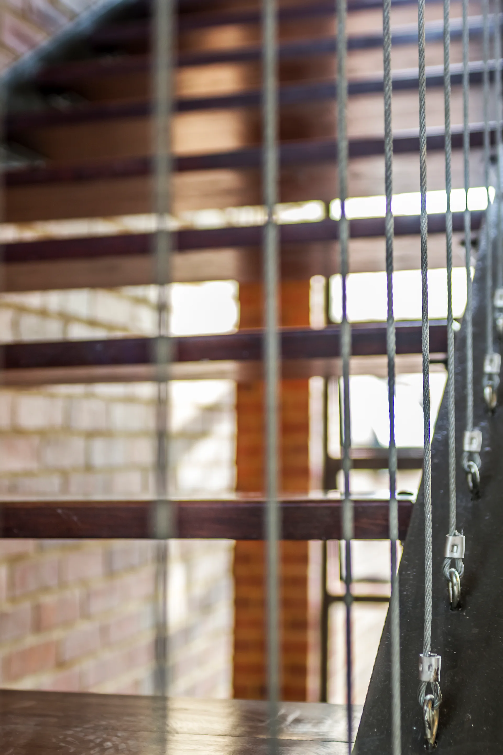 Close-up of an open riser staircase with dark wood treads and vertical steel cable railings in front of an exposed brick wall.