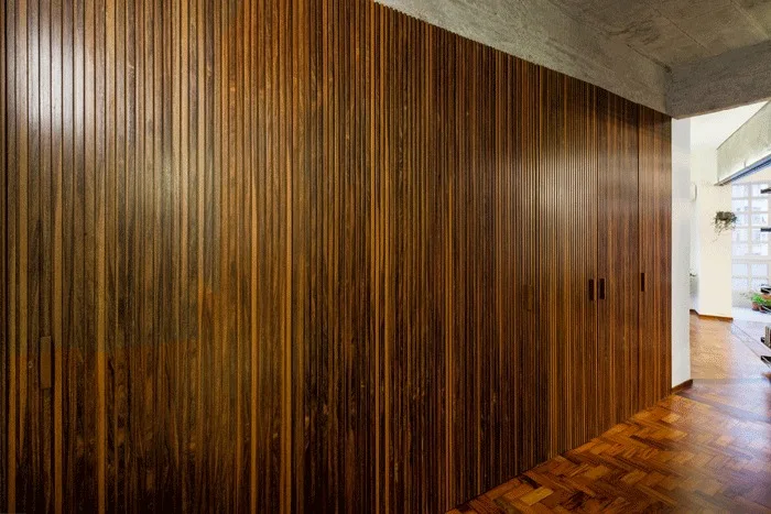 A hallway featuring a floor-to-ceiling slatted wood wall of integrated cabinetry next to herringbone parquet flooring and an exposed concrete ceiling.