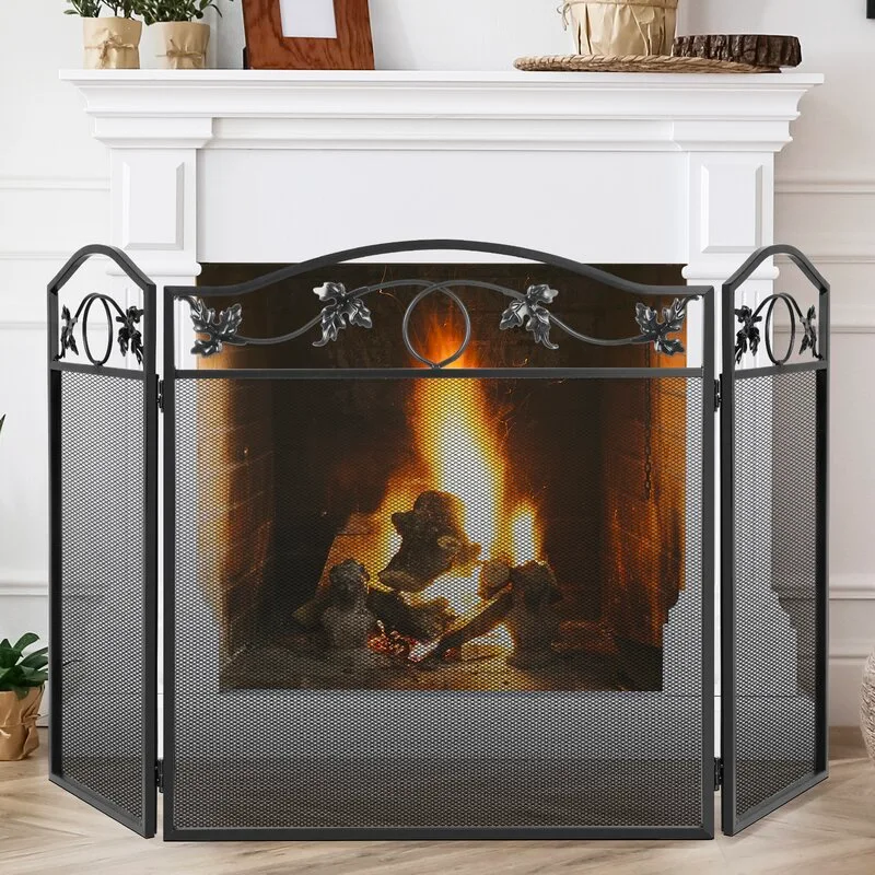 A three-panel black metal fire screen with decorative leaf motifs stands in front of a glowing fireplace with a white wooden mantel.