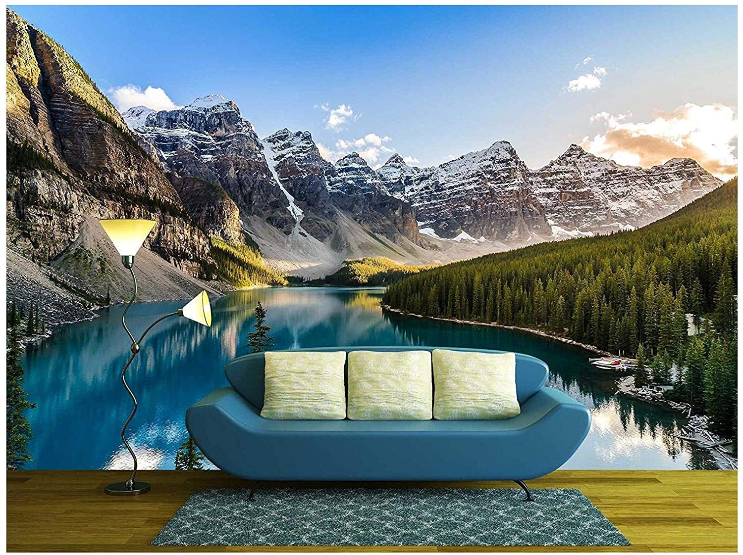 A blue curved sofa with patterned yellow pillows sits on a textured rug in front of a large mountain lake wall mural.