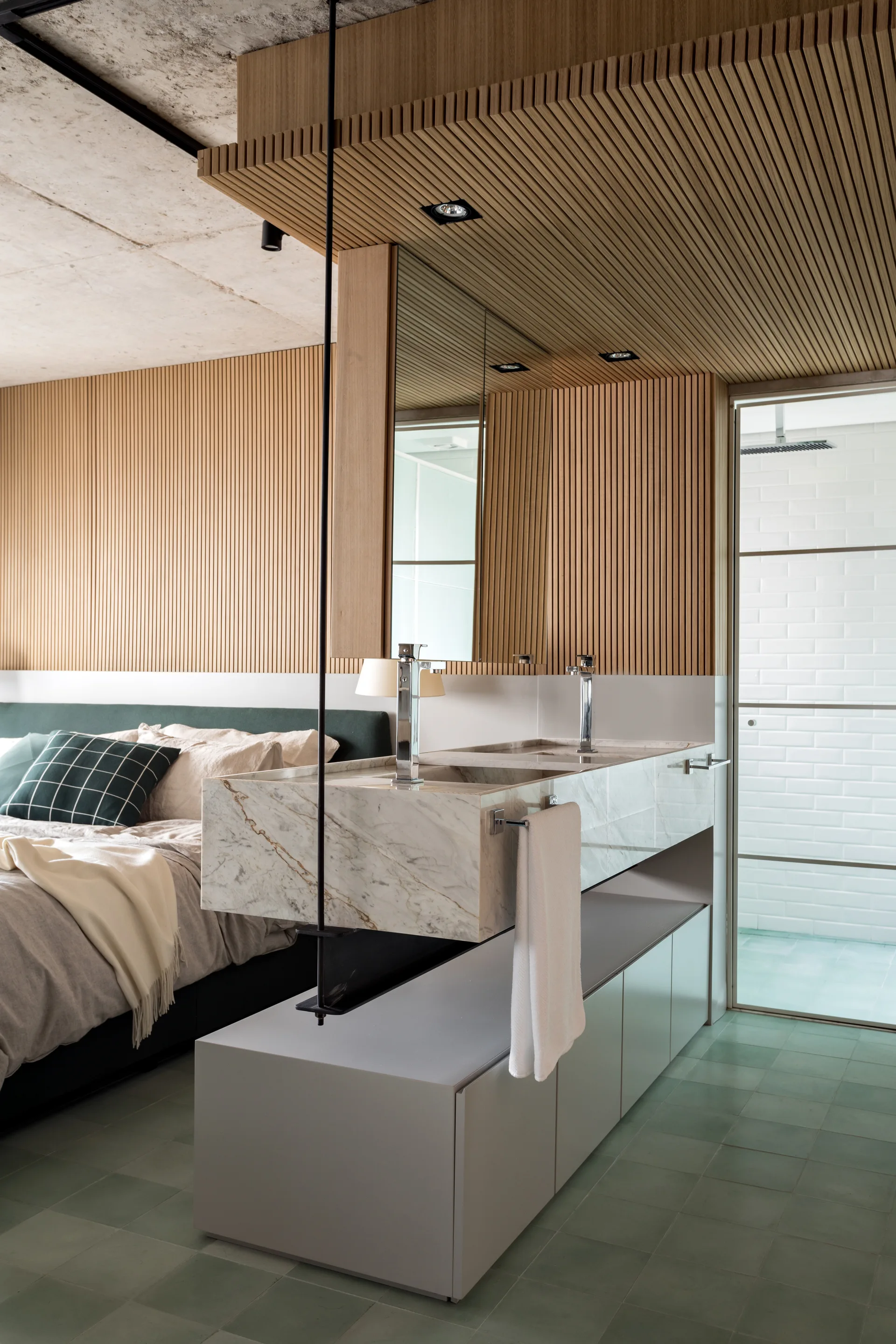 A modern bedroom features a floating marble vanity, slatted wood wall paneling, a bed with green accents, and green tiled flooring.