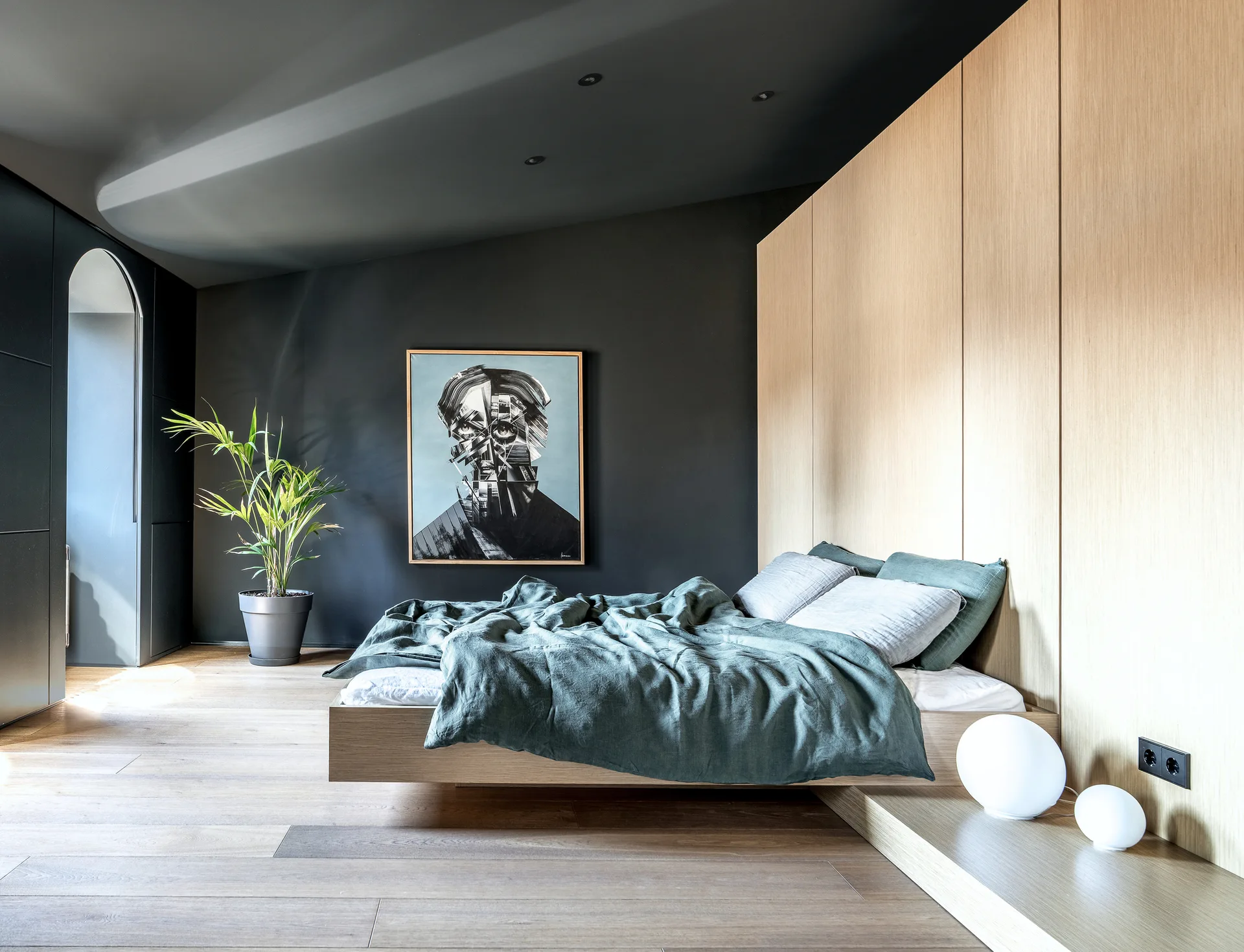 A modern minimalist bedroom features a floating wooden platform bed set against light oak wall paneling and a dark charcoal gray wall.