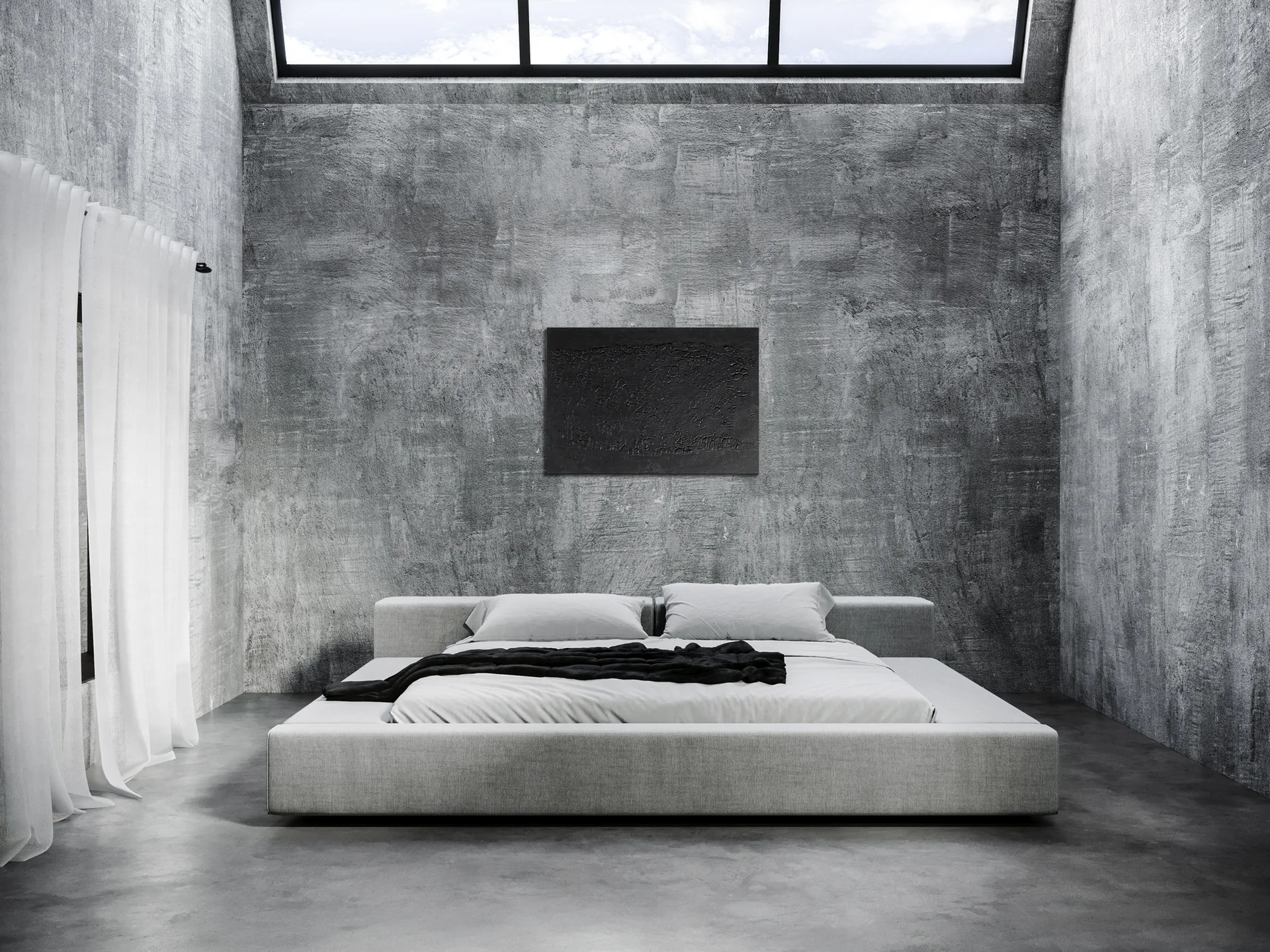 A low-profile gray platform bed is centered in a minimalist bedroom with textured concrete walls, a dark canvas artwork, and an overhead skylight.