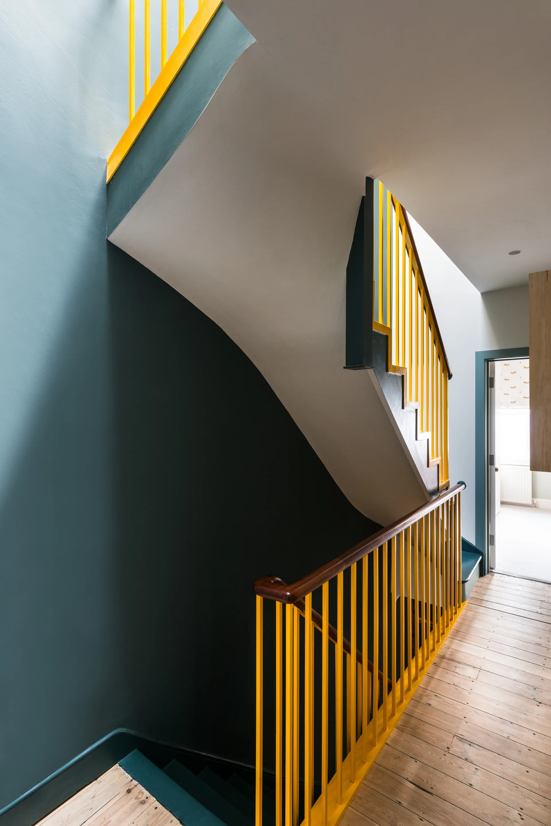 A multi-story staircase features vibrant yellow railings, dark teal painted walls, a natural wood handrail, and light wood plank flooring.