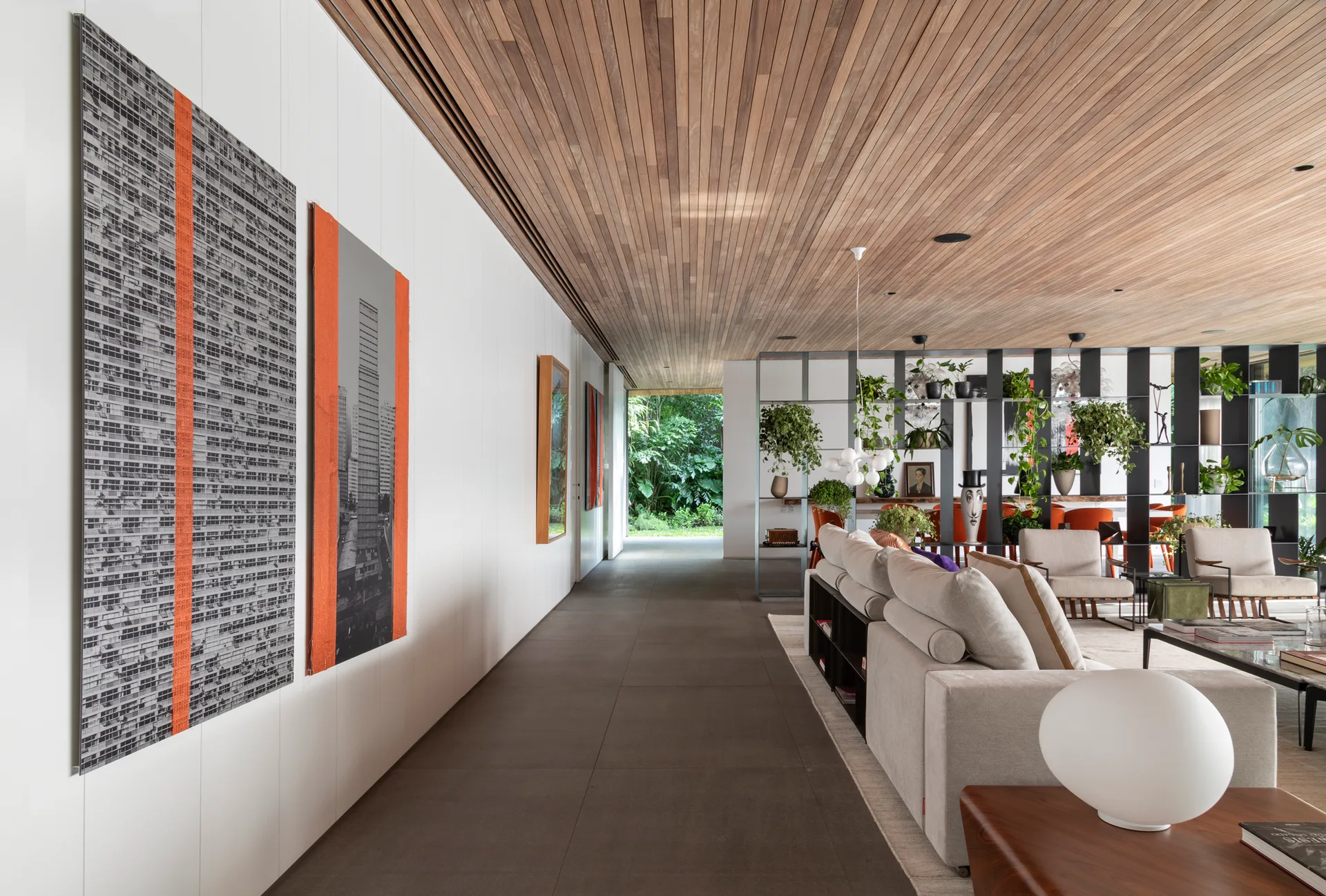 A modern living room featuring a warm wood-slat ceiling, large graphic art on a white paneled wall, and a cream sofa beside an open metal room divider.