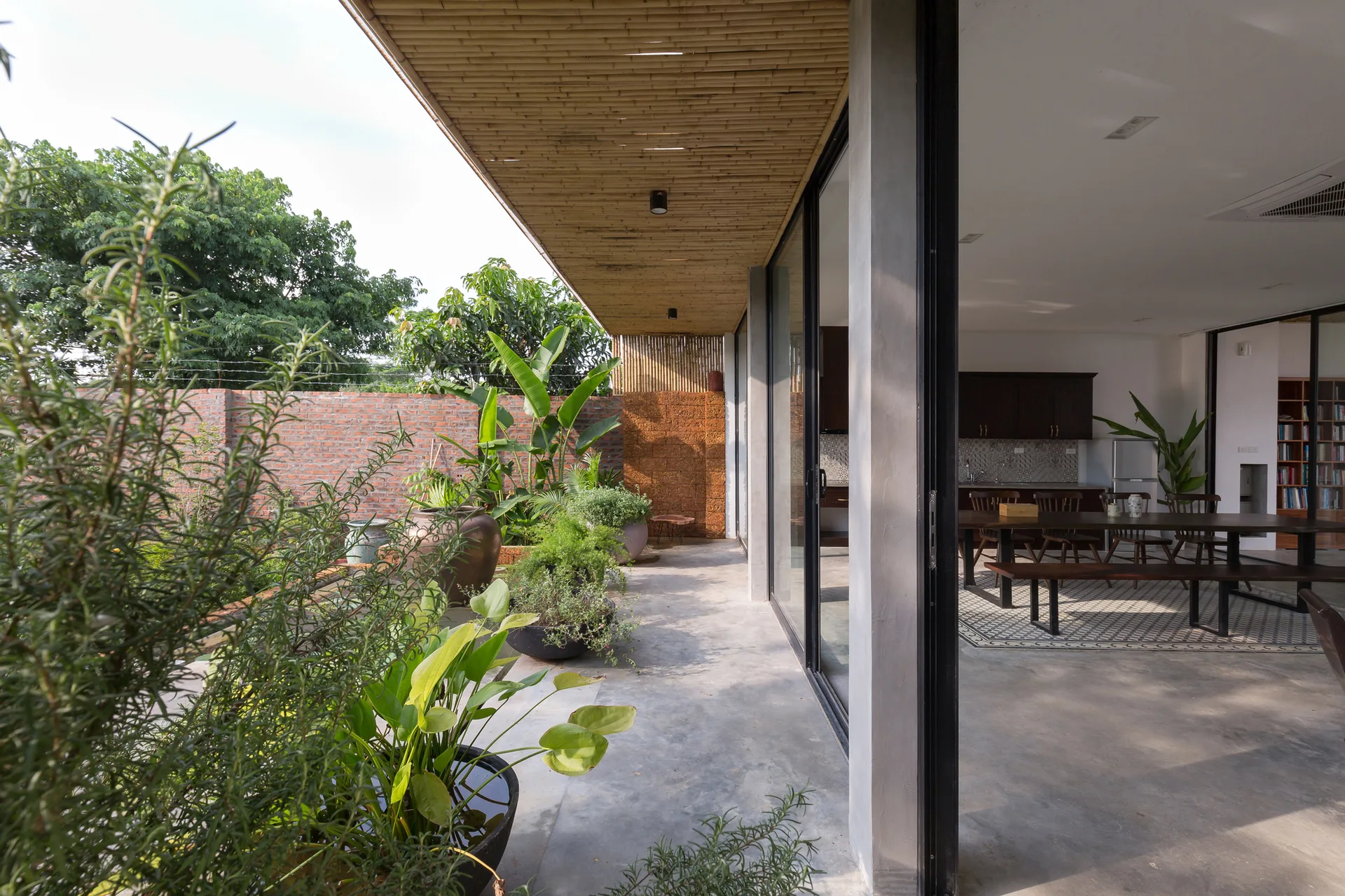 A covered concrete patio with a slatted bamboo ceiling, potted plants, and large sliding glass doors leading to an indoor dining room.