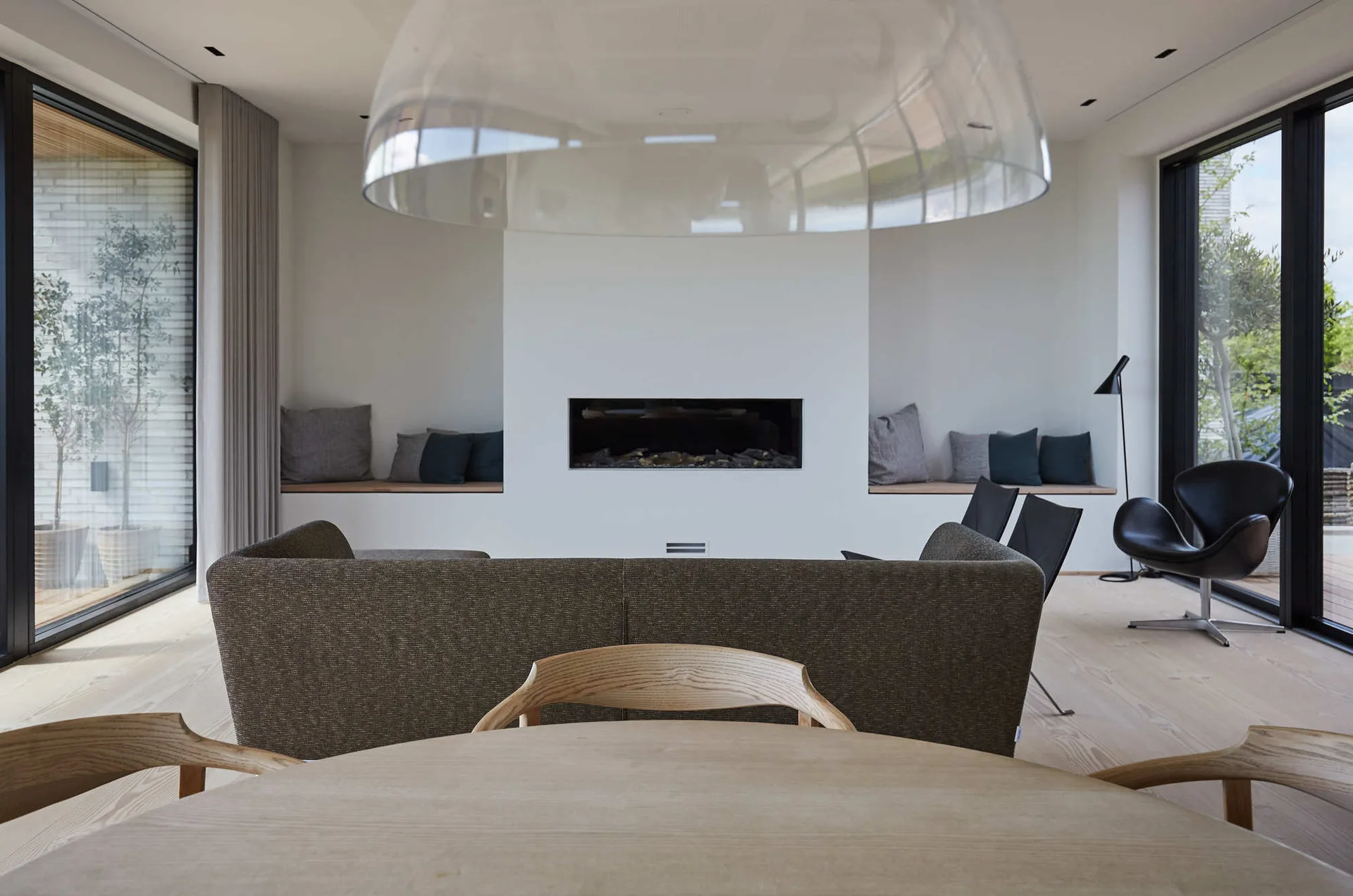 A minimalist living room features a built-in linear fireplace flanked by recessed wooden benches with cushions and a brown sofa.