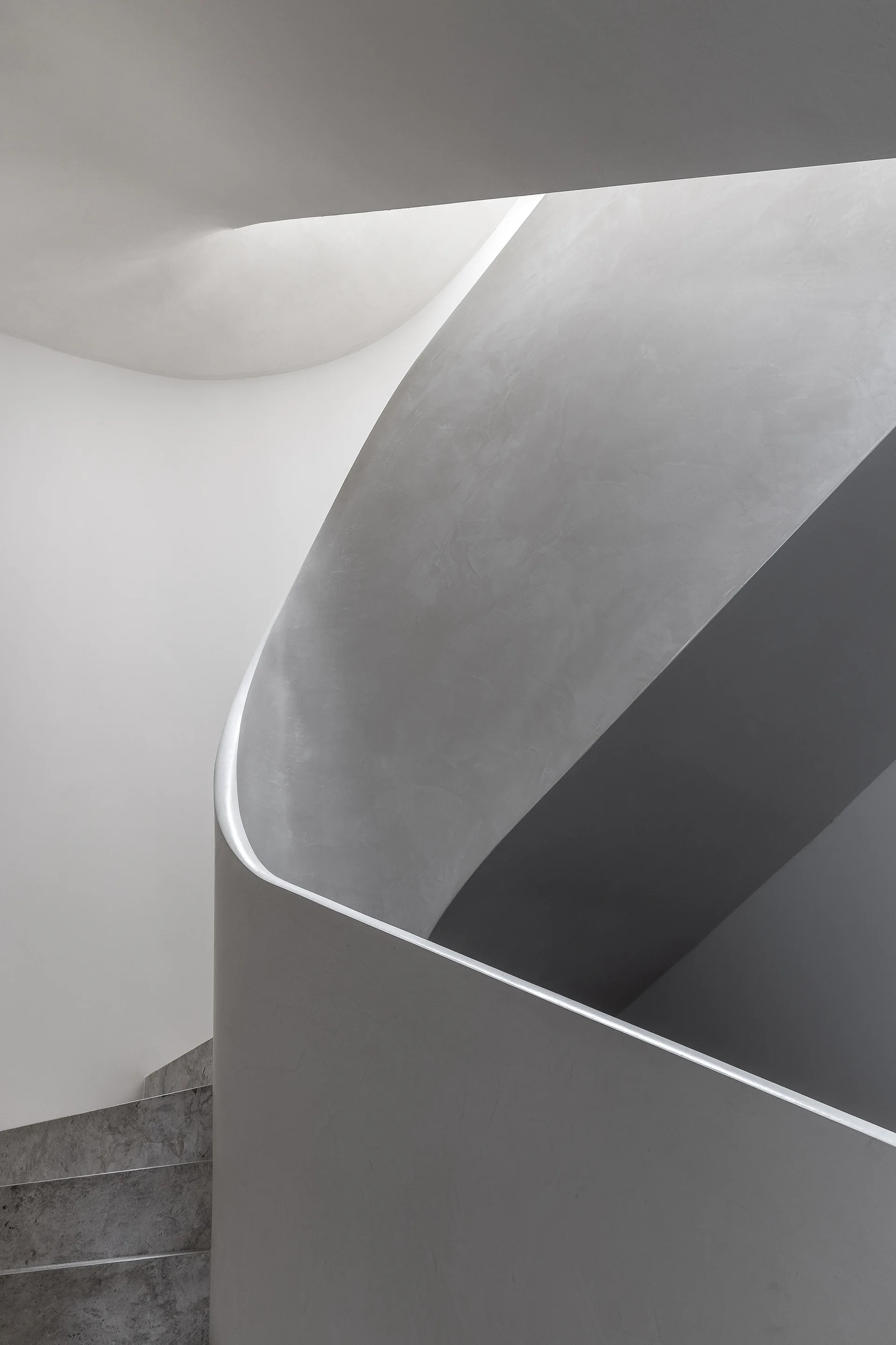 A curved gray plaster staircase features textured stone treads and a sweeping, smooth balustrade.