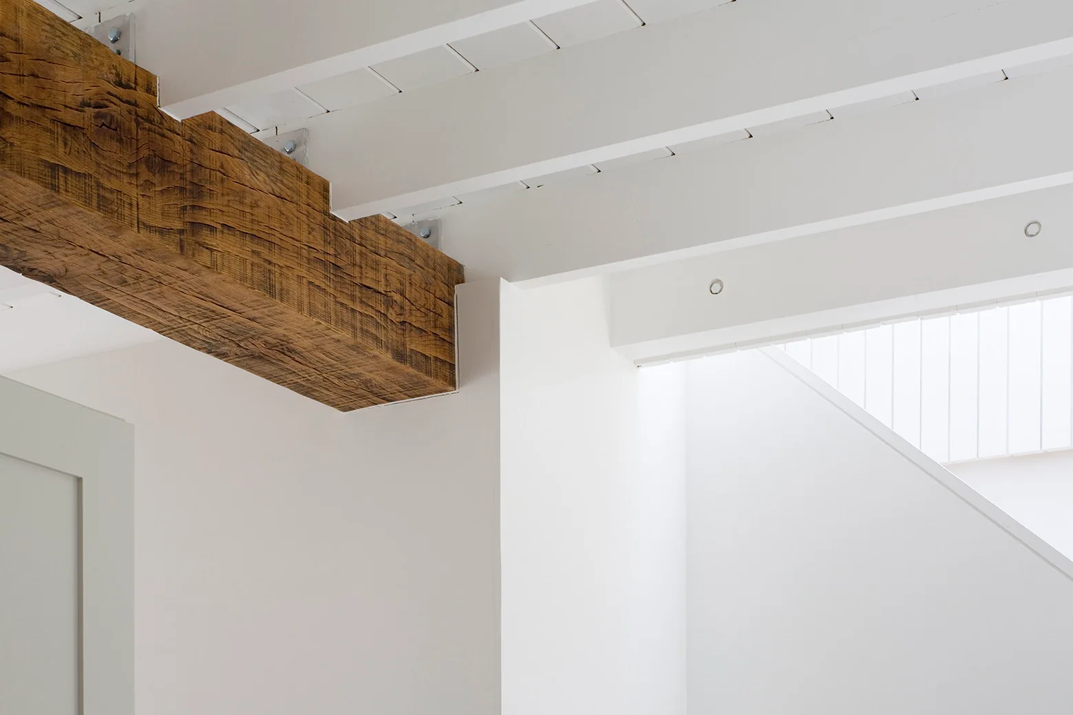 A rustic brown timber beam contrasts with white painted ceiling joists and clean walls in a minimalist interior.