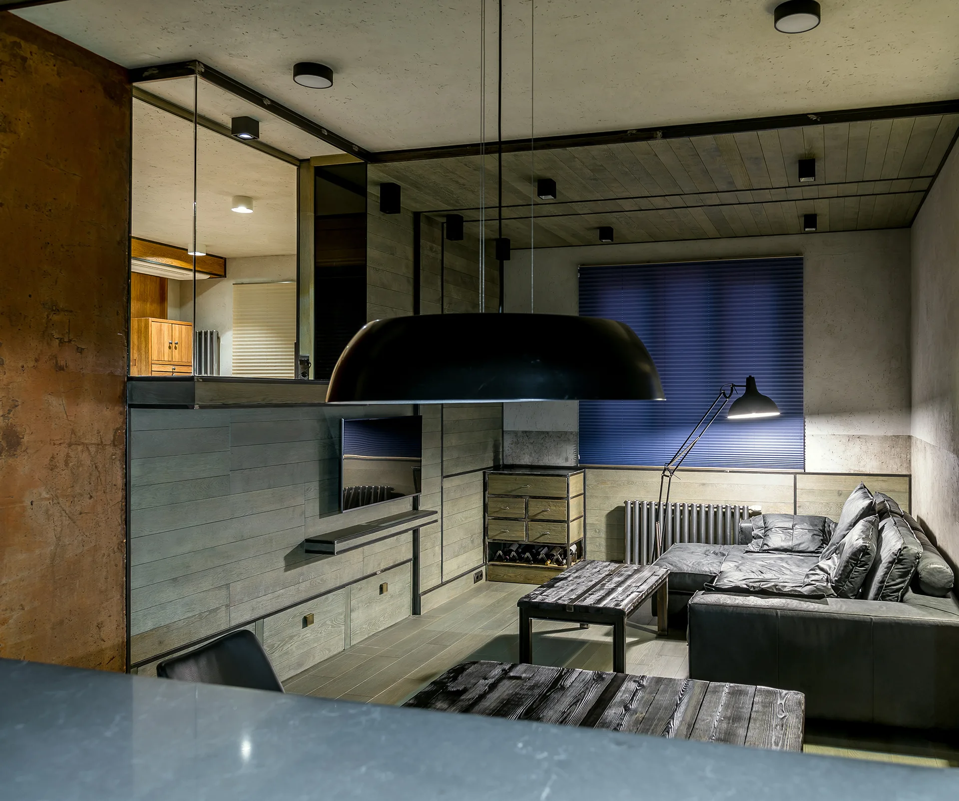 A modern industrial living room featuring a dark leather sectional sofa, rustic wood coffee tables, and gray planked walls.