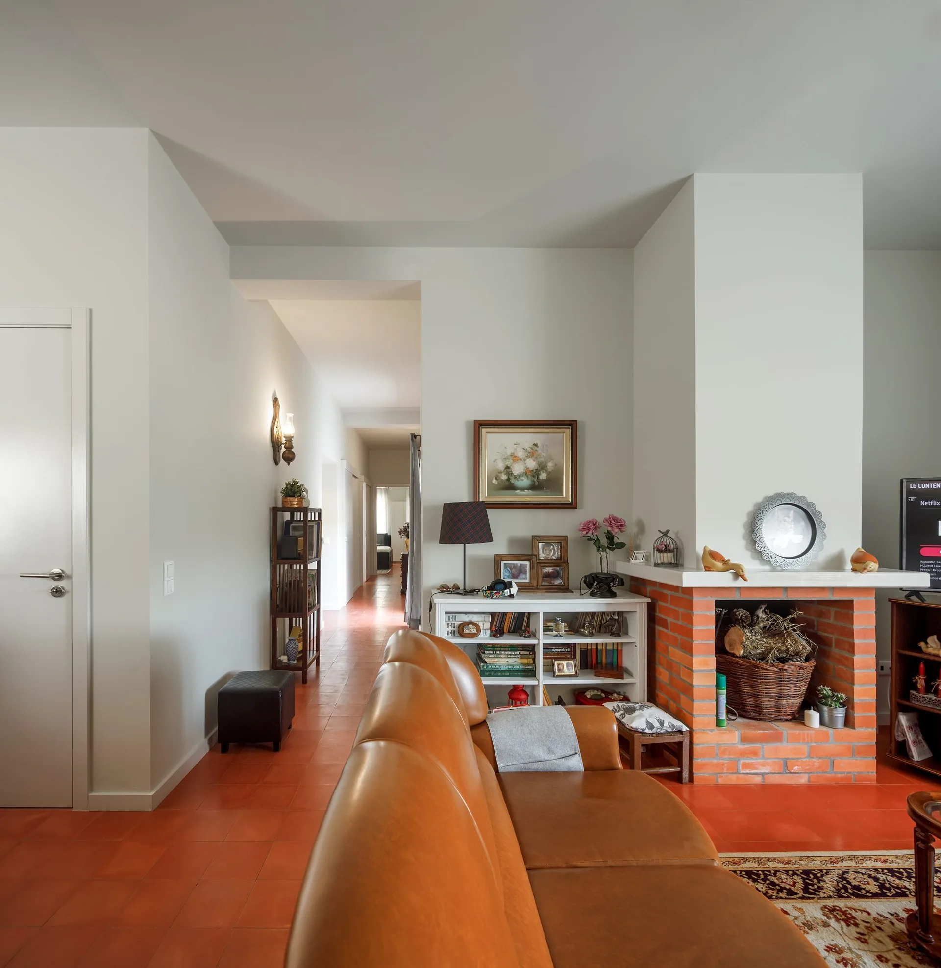 A living room features a brown leather sofa in the foreground, a brick fireplace, and reddish-brown terracotta tile floors.