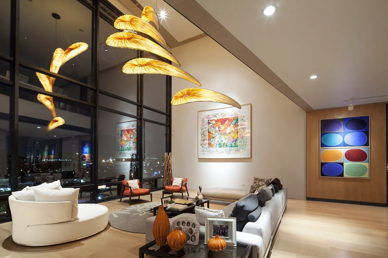 A contemporary living room featuring a modular sofa, colorful abstract artwork, and a large sculptural amber pendant light hanging near tall windows at night.