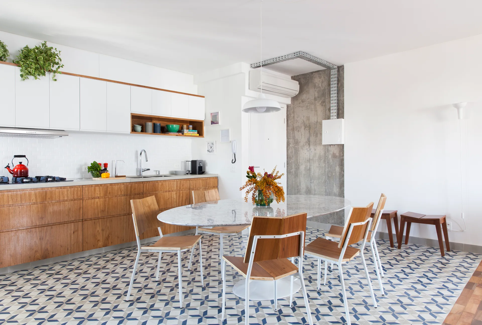 A modern open kitchen and dining space with wooden cabinets, a marble oval table, wood chairs, and blue geometric floor tiles.