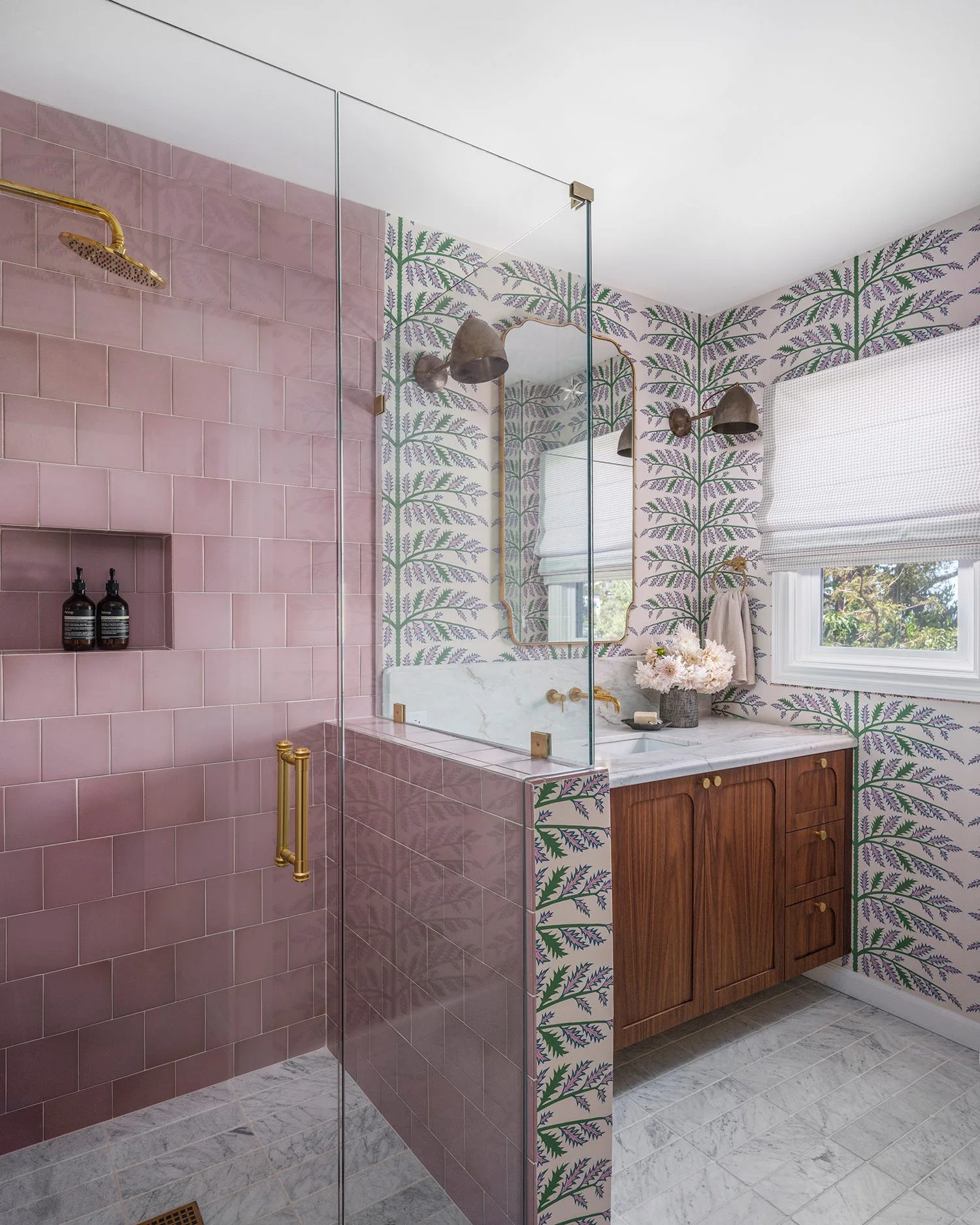 A bathroom featuring a glass shower with pink tiles, a wooden vanity with marble countertop, and botanical print wallpaper.