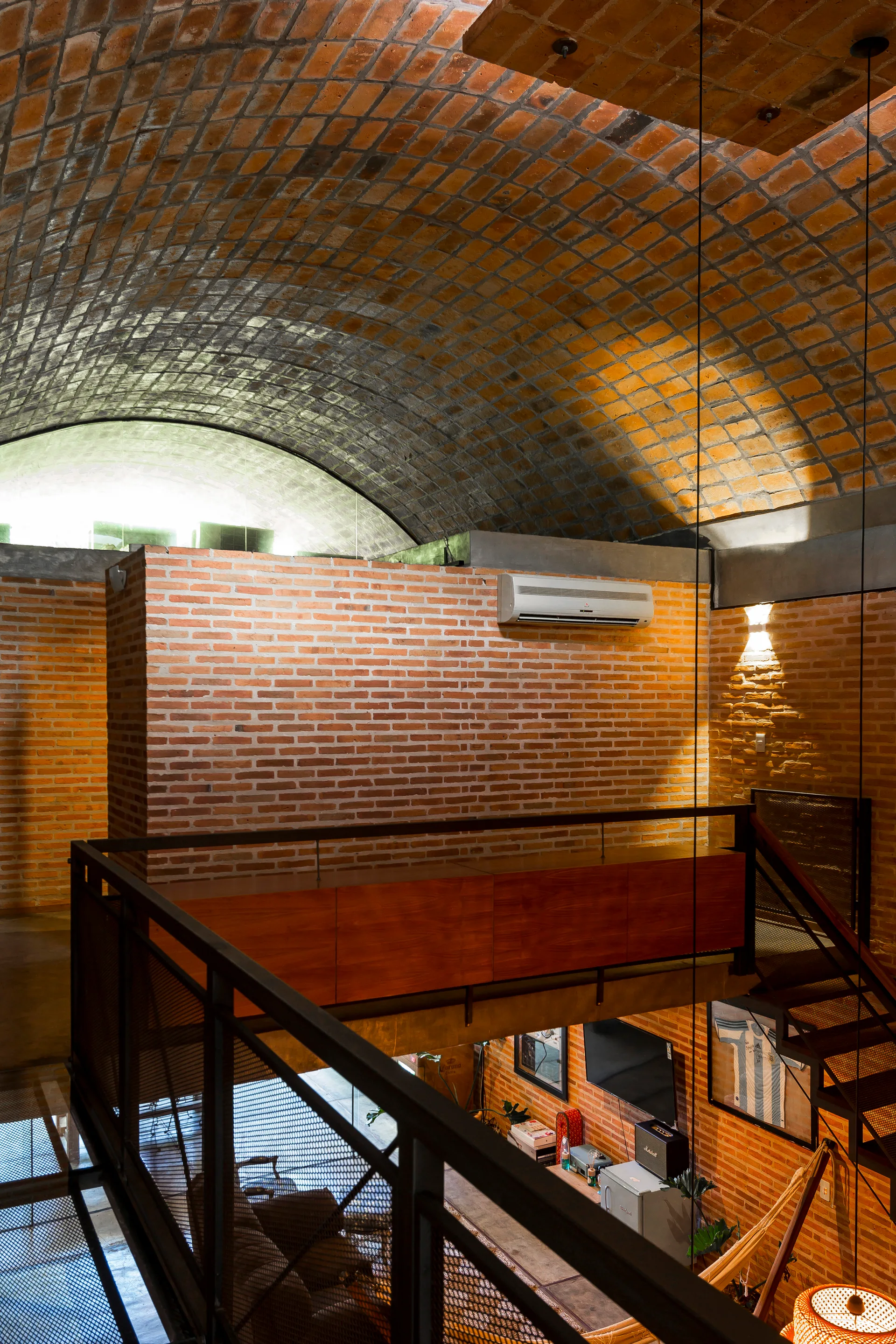 A multi-level industrial loft features a curved barrel-vaulted brick ceiling, exposed red brick walls, and a metal mesh mezzanine railing.
