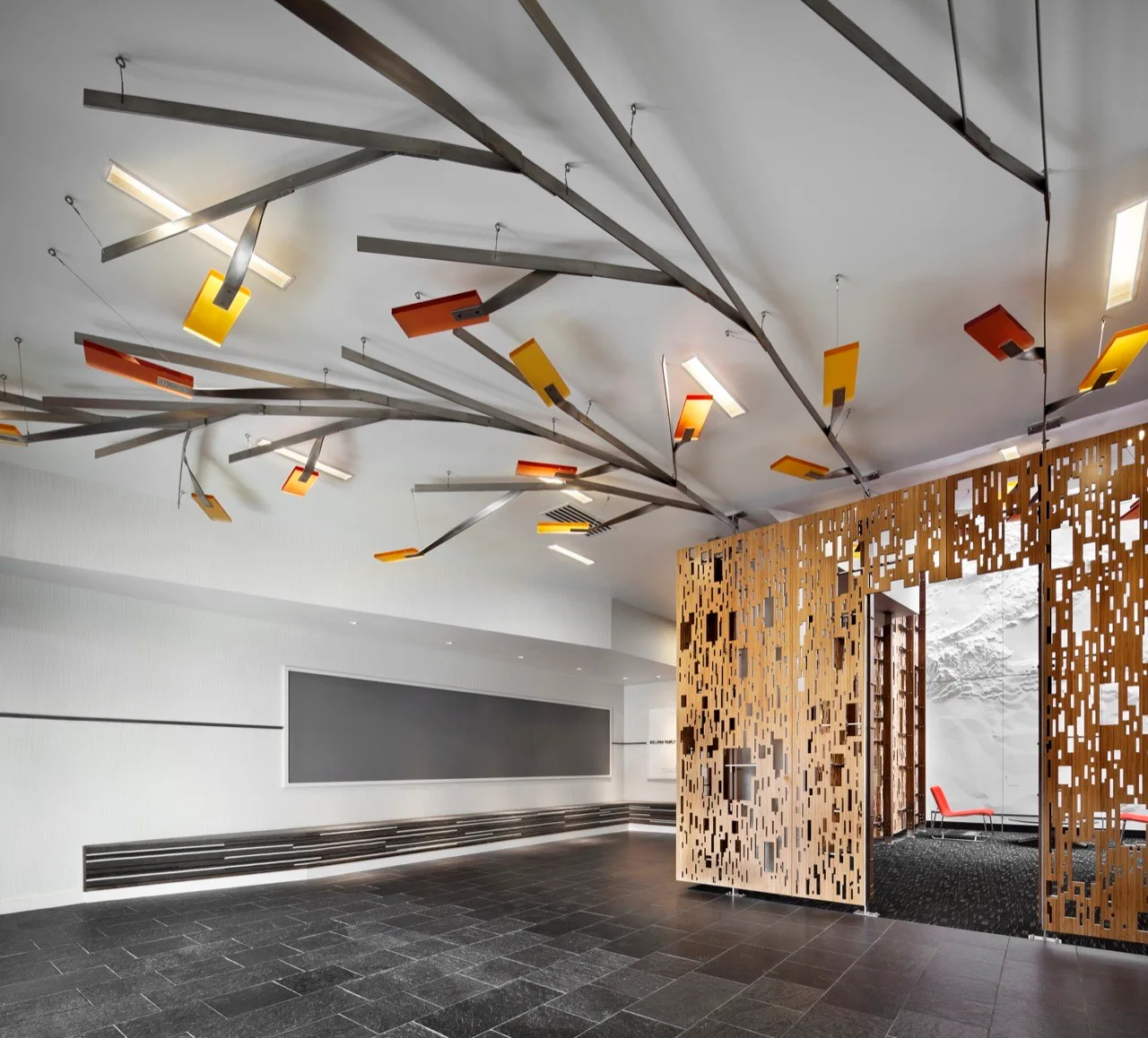 A modern commercial entryway features a large branching metal ceiling light installation and an intricate geometric cut-out wooden room divider.