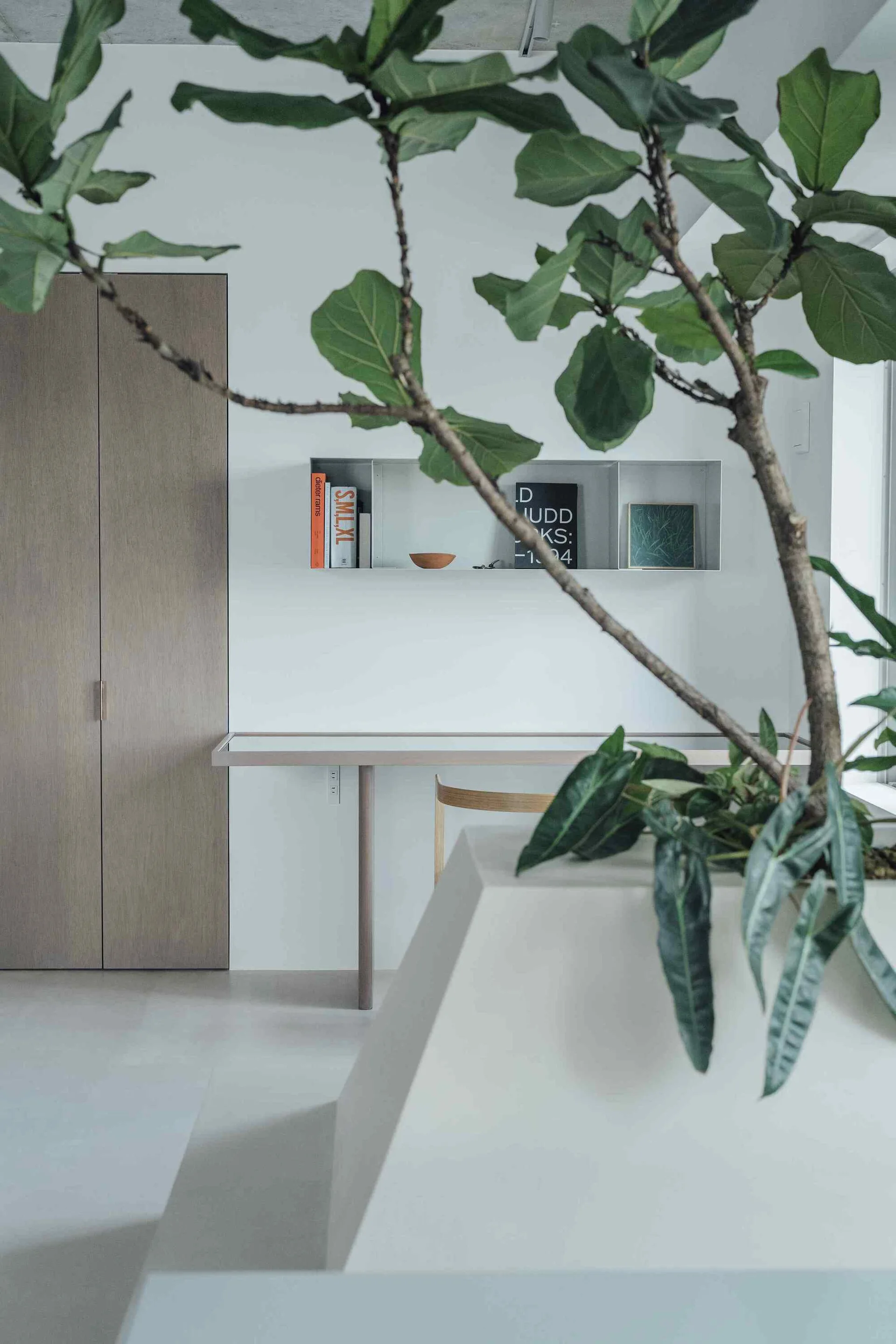 A minimalist desk area features a light wood cabinet, a slim console table, and a metal floating wall shelf styled with books.