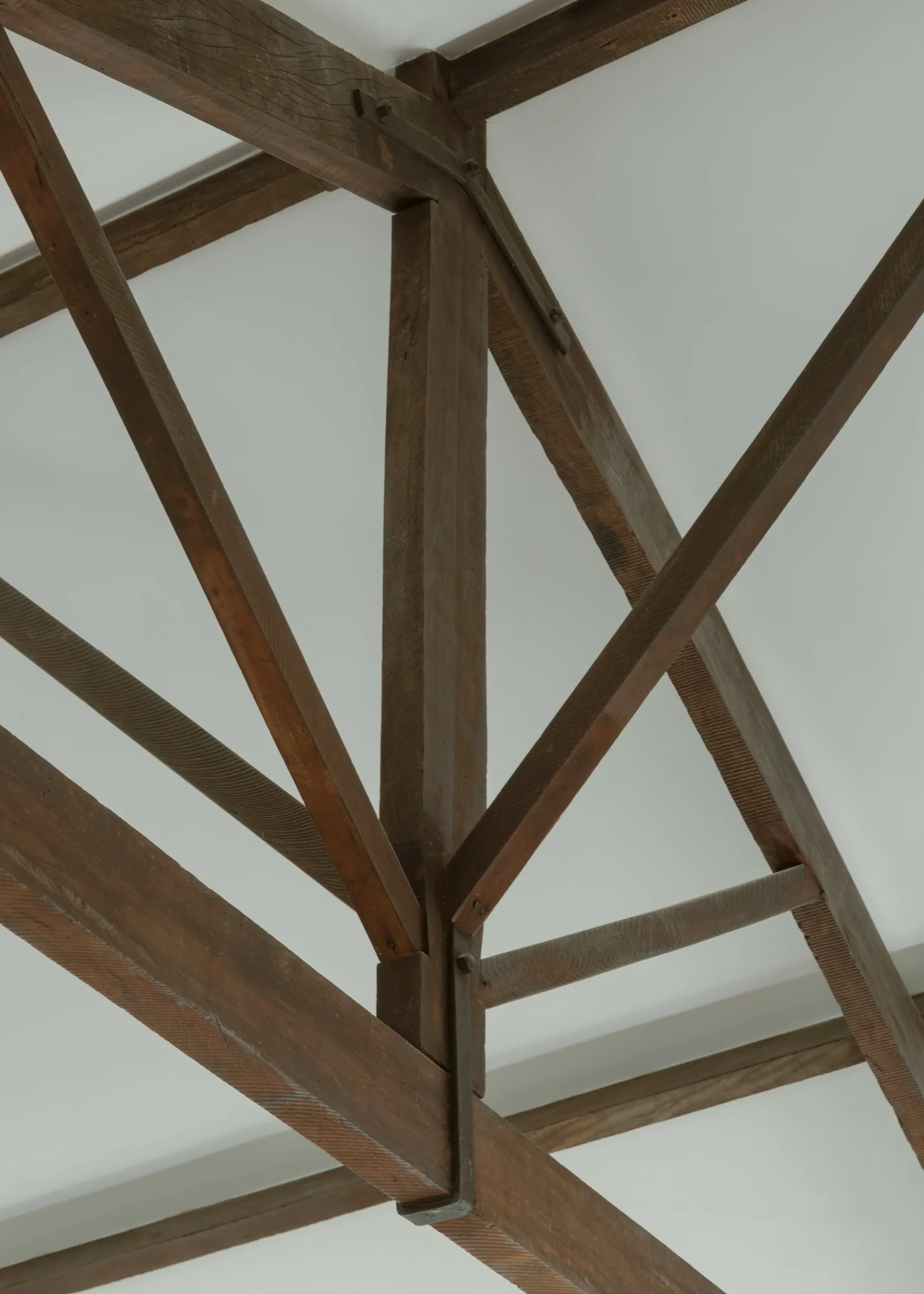 A close-up of dark-stained wooden structural ceiling beams forming a geometric truss against a flat white ceiling.